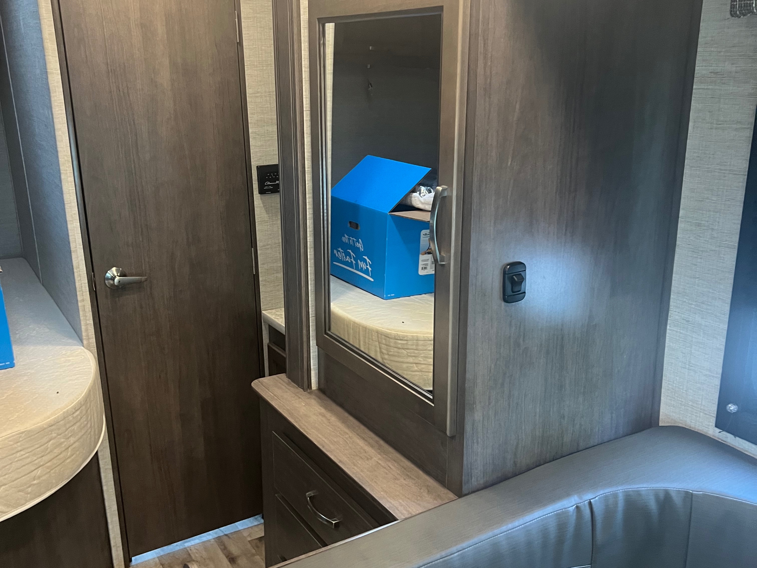 Compact RV rental interior with vanity mirror reflecting a blue box, adjacent to a door, storage drawers, and bench seating.. Jayco Redhawk SE 2023