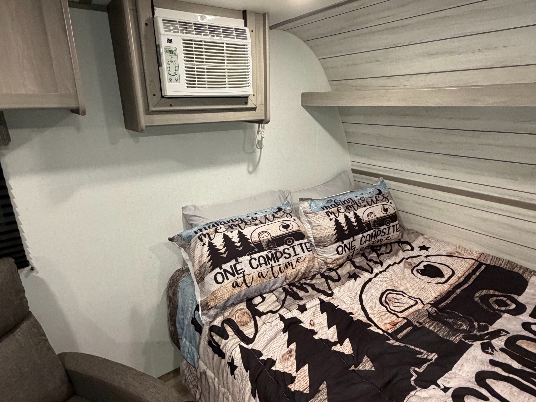 Cozy RV rental bedroom featuring a window AC unit, "making memories" themed bedding, and light wood paneling.. Dutchmen Coleman 2024