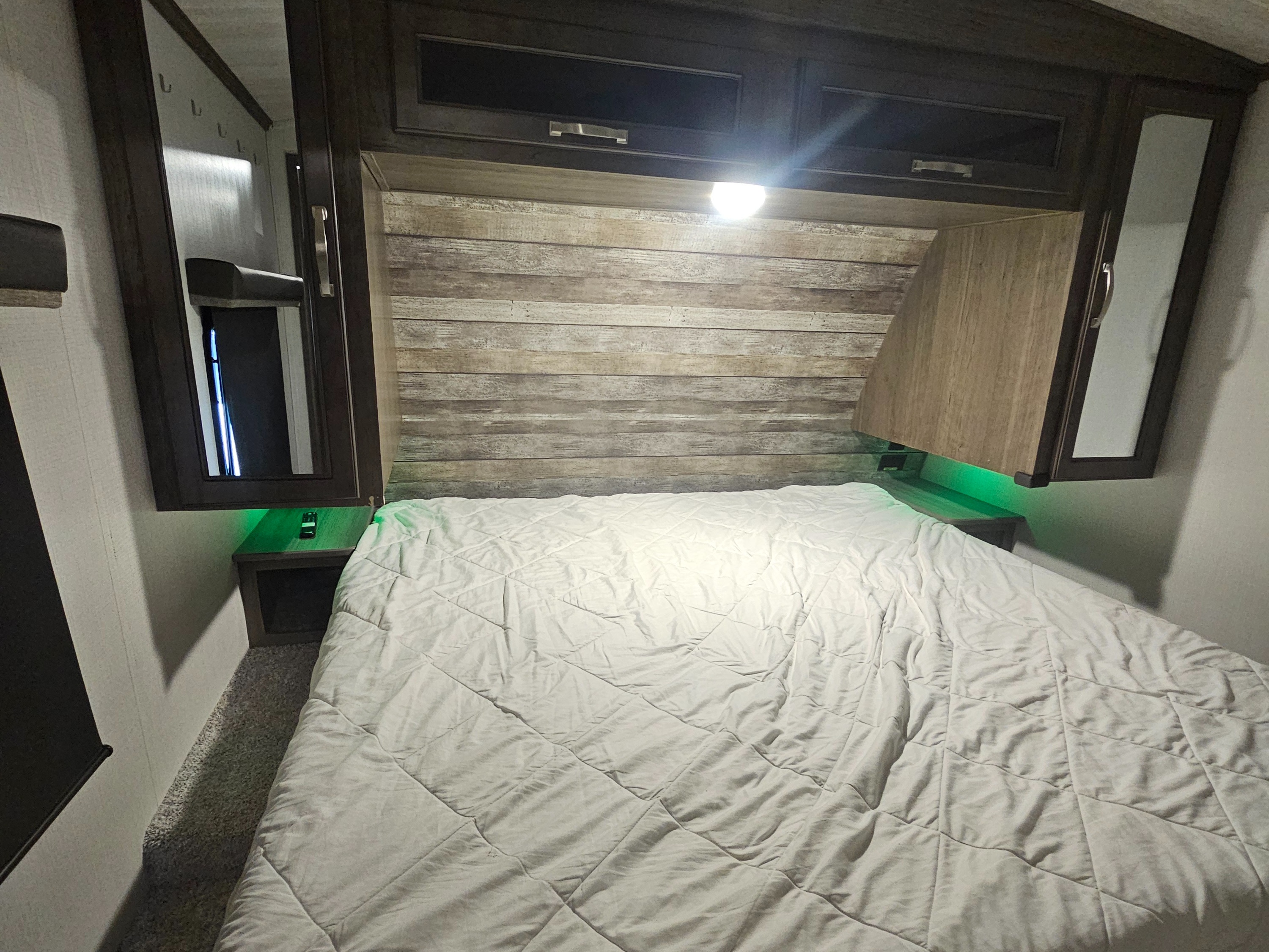 Cozy RV rental bedroom with overhead storage, mirrored cabinets, and ambient green lighting around the bed.. Keystone RV Cougar 2022