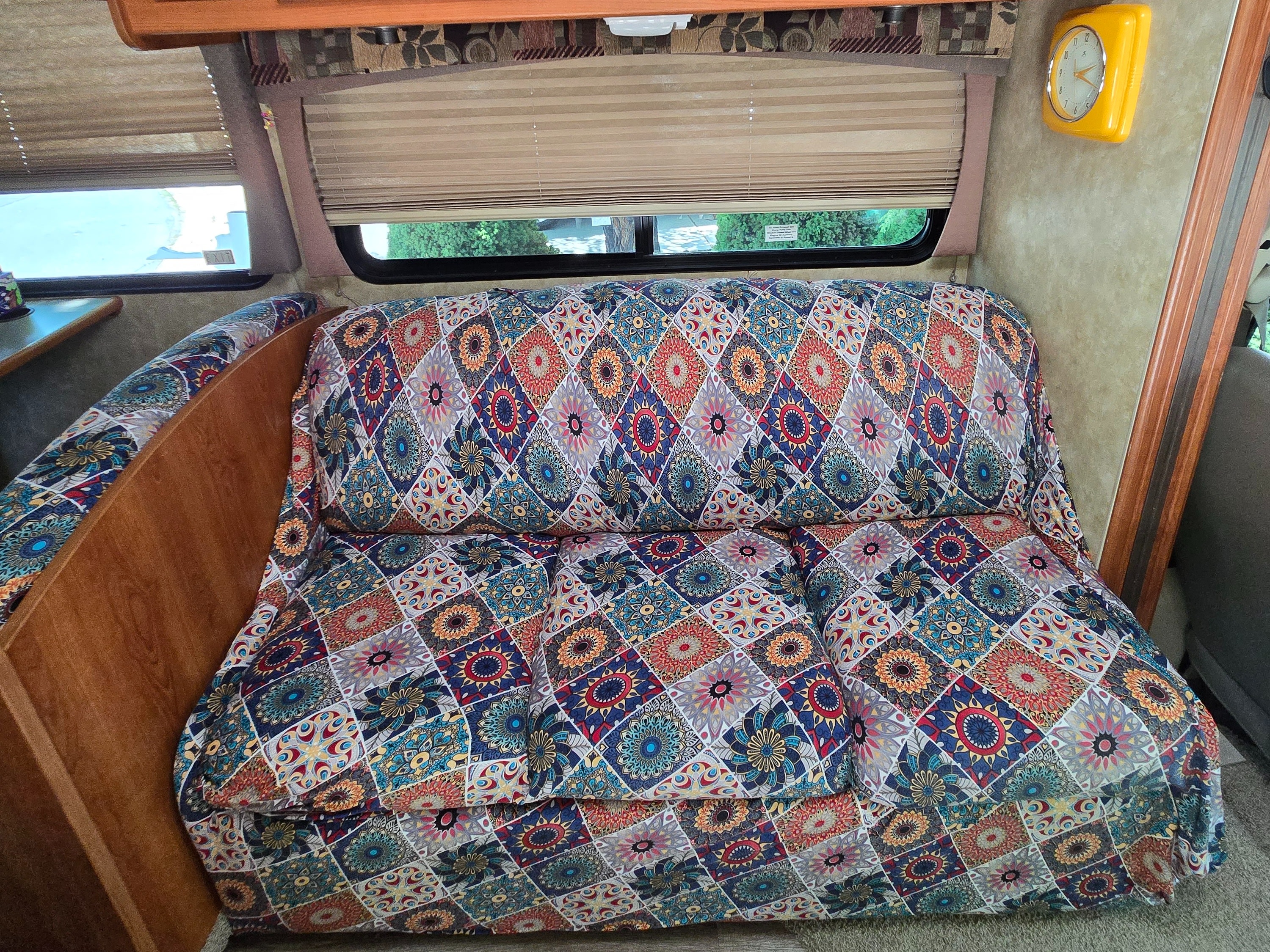 Vibrant patterned sofa and window blinds inside this RV rental, with a yellow wall clock on the right.. Coachmen Freedom Express 2008