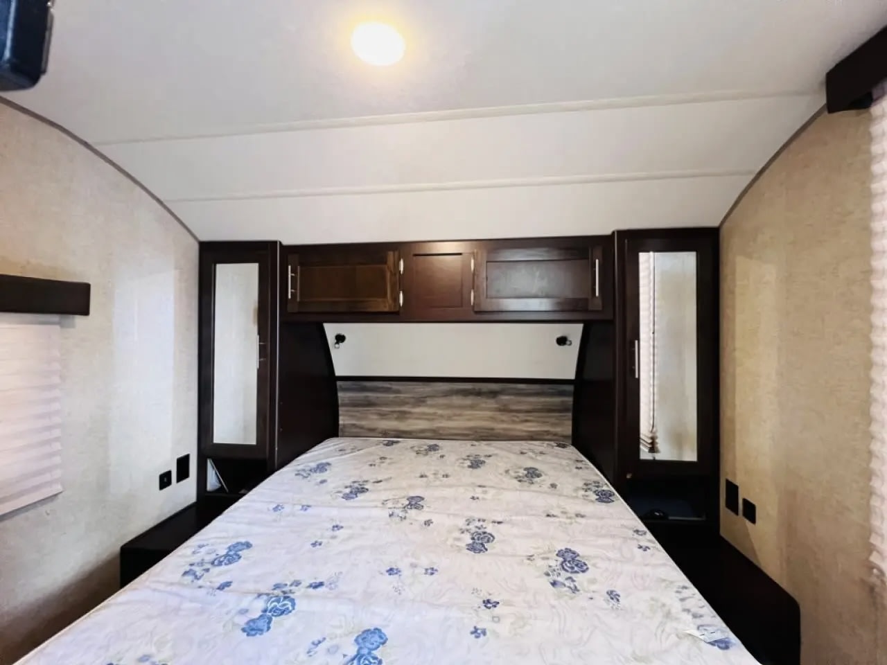 Cozy RV rental bedroom featuring a bed with floral duvet, overhead cabinets, and mirrored storage for travel.. Forest River Cherokee Grey Wolf 2019