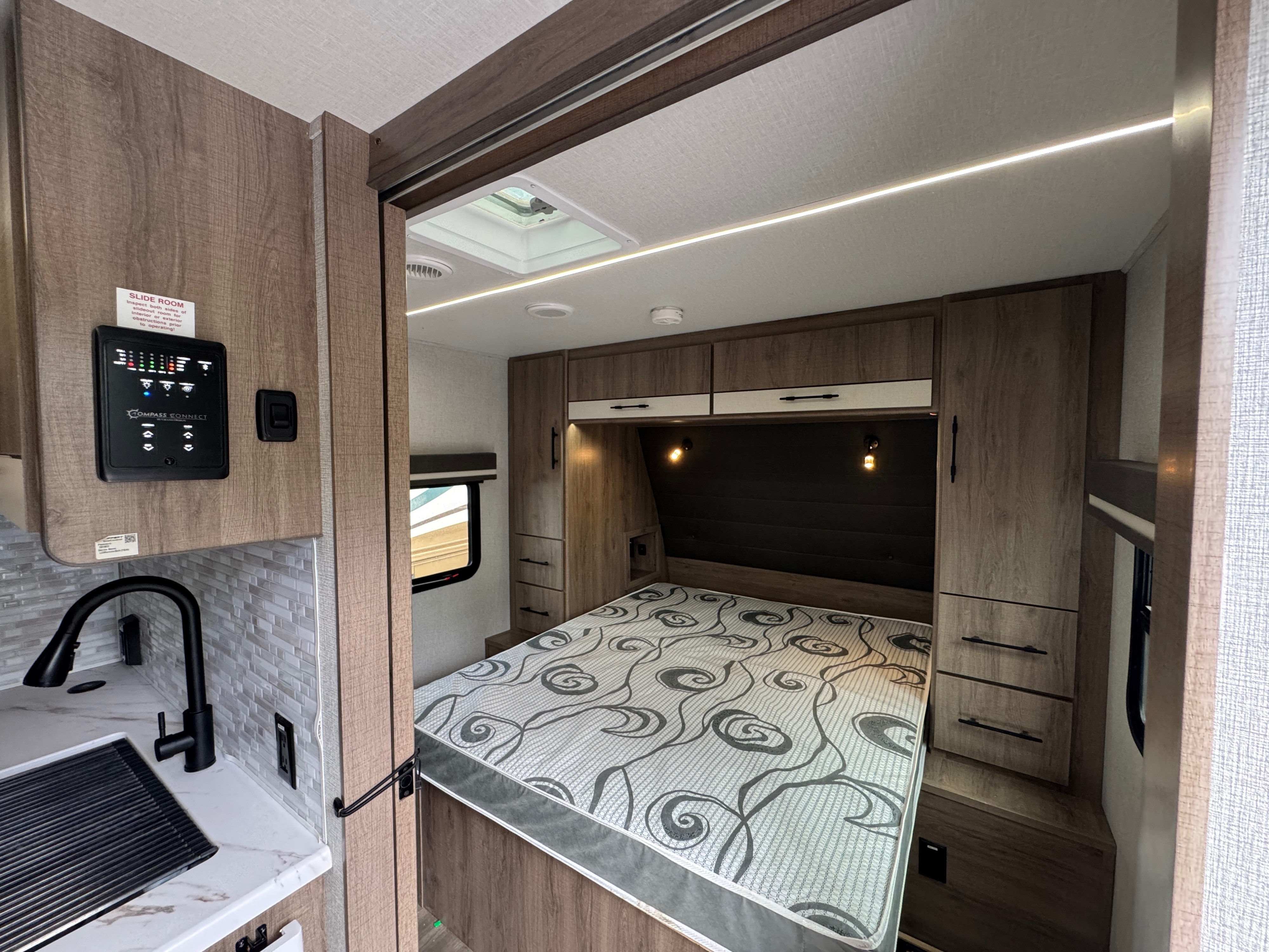 Stylish RV rental interior: cozy bedroom with modern lighting, ample storage, and a control panel for convenience.. Grand Design Imagine XLS 2024