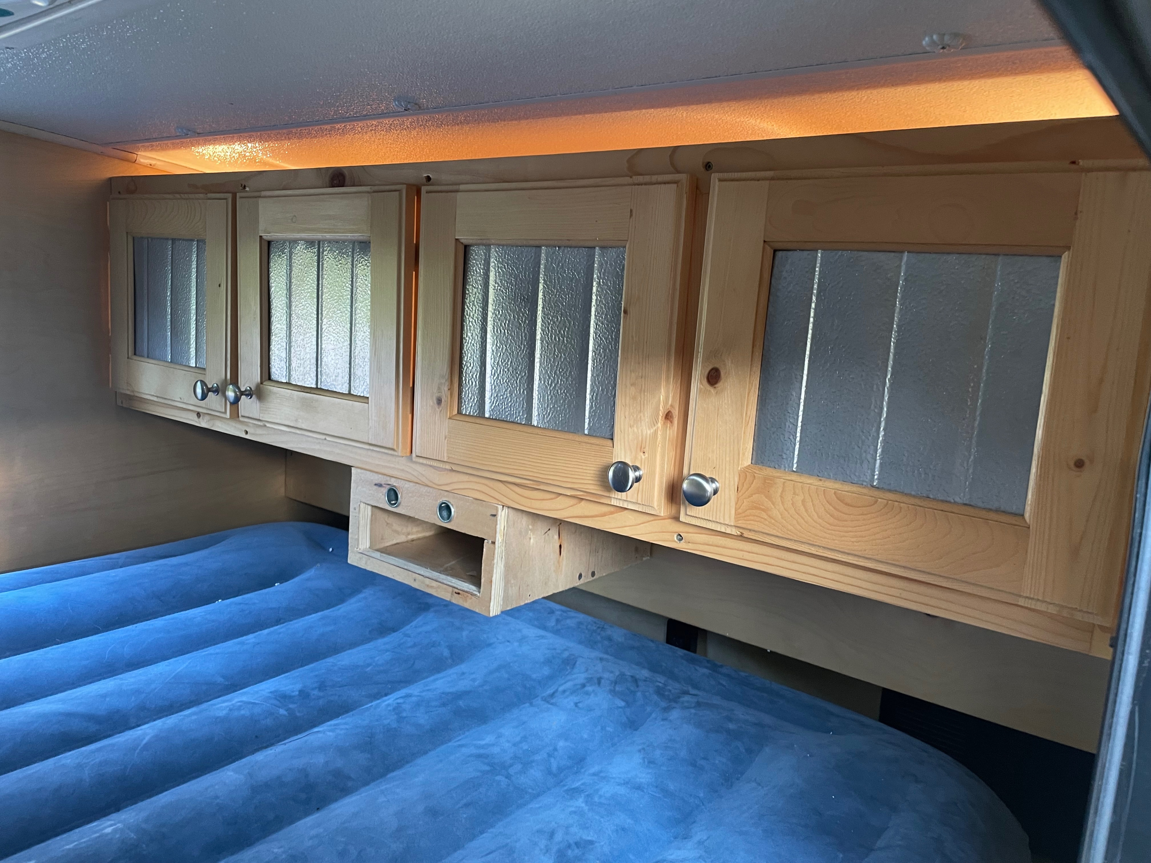 Cozy RV rental bedroom featuring wooden cabinets, ambient lighting, and an inflatable bed for comfortable travel.. hand built teardrop 2016
