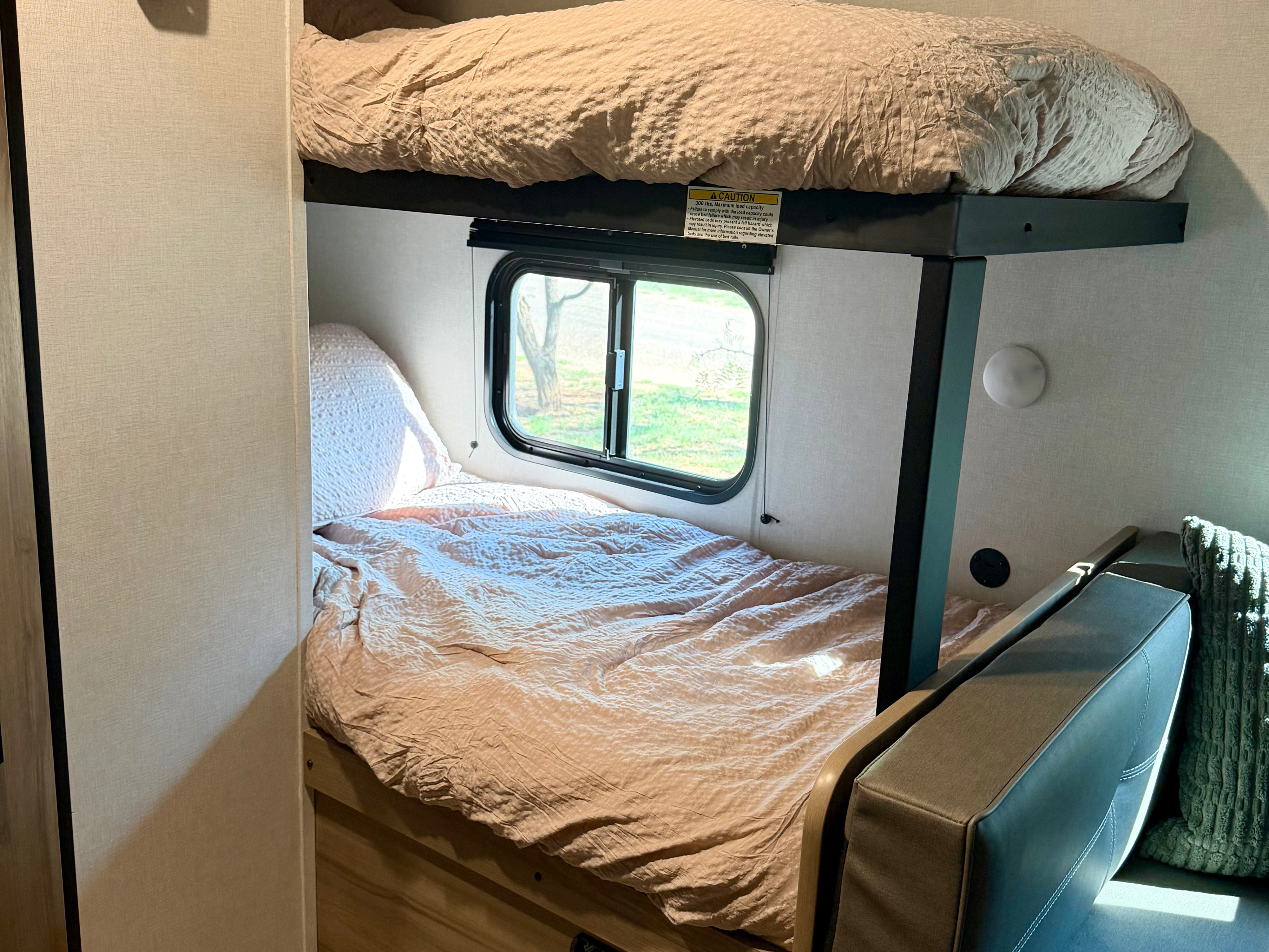 RV rental interior showing cozy bunk beds with window and seating. Top bunk max load 300 lbs for family camping.. Keystone RV Coleman 2026