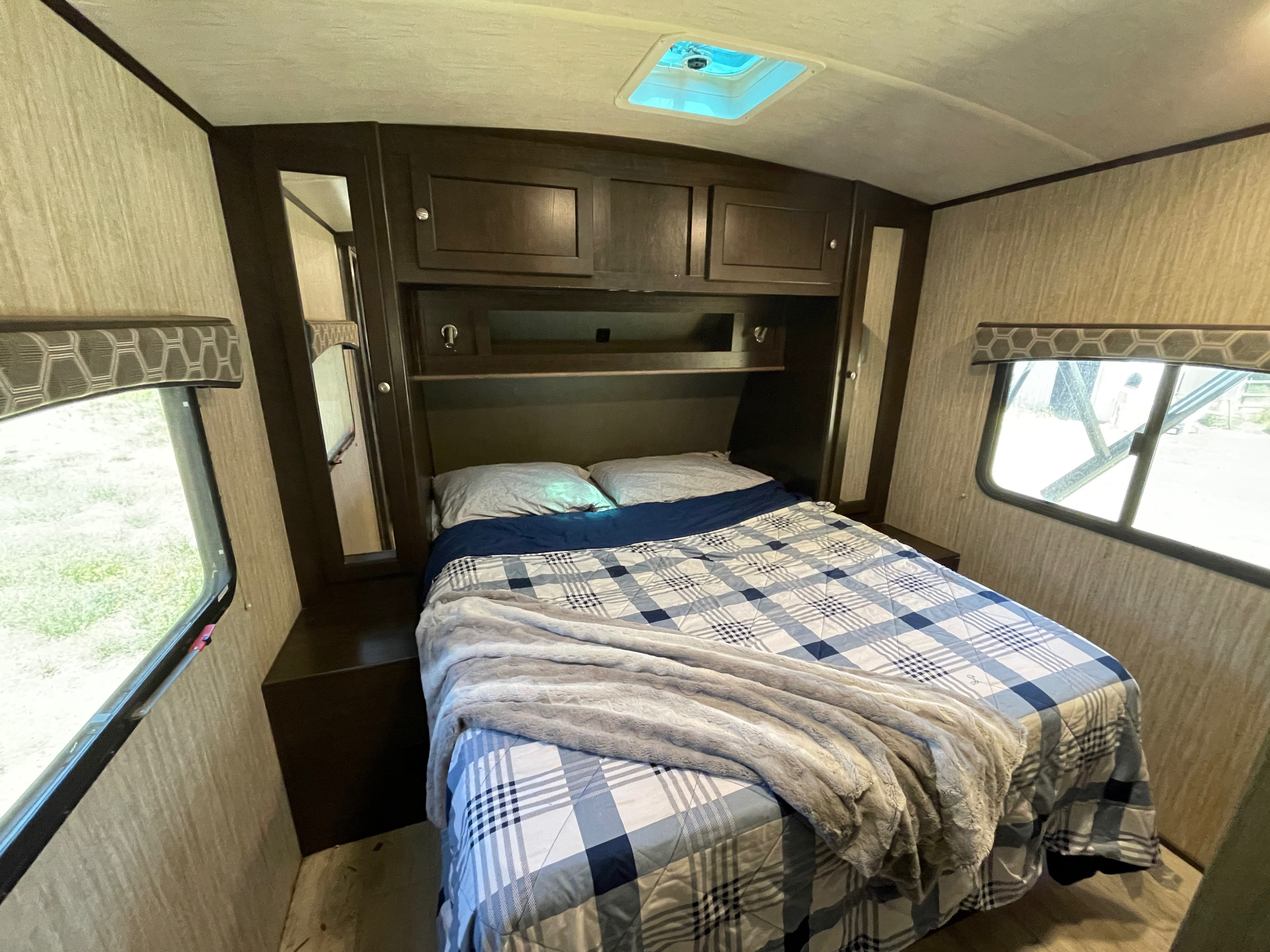Inside a cozy RV rental bedroom: a comfy bed with plaid bedding, overhead storage, and windows offering natural light.. Cruiser RV Shadow Cruiser 2019