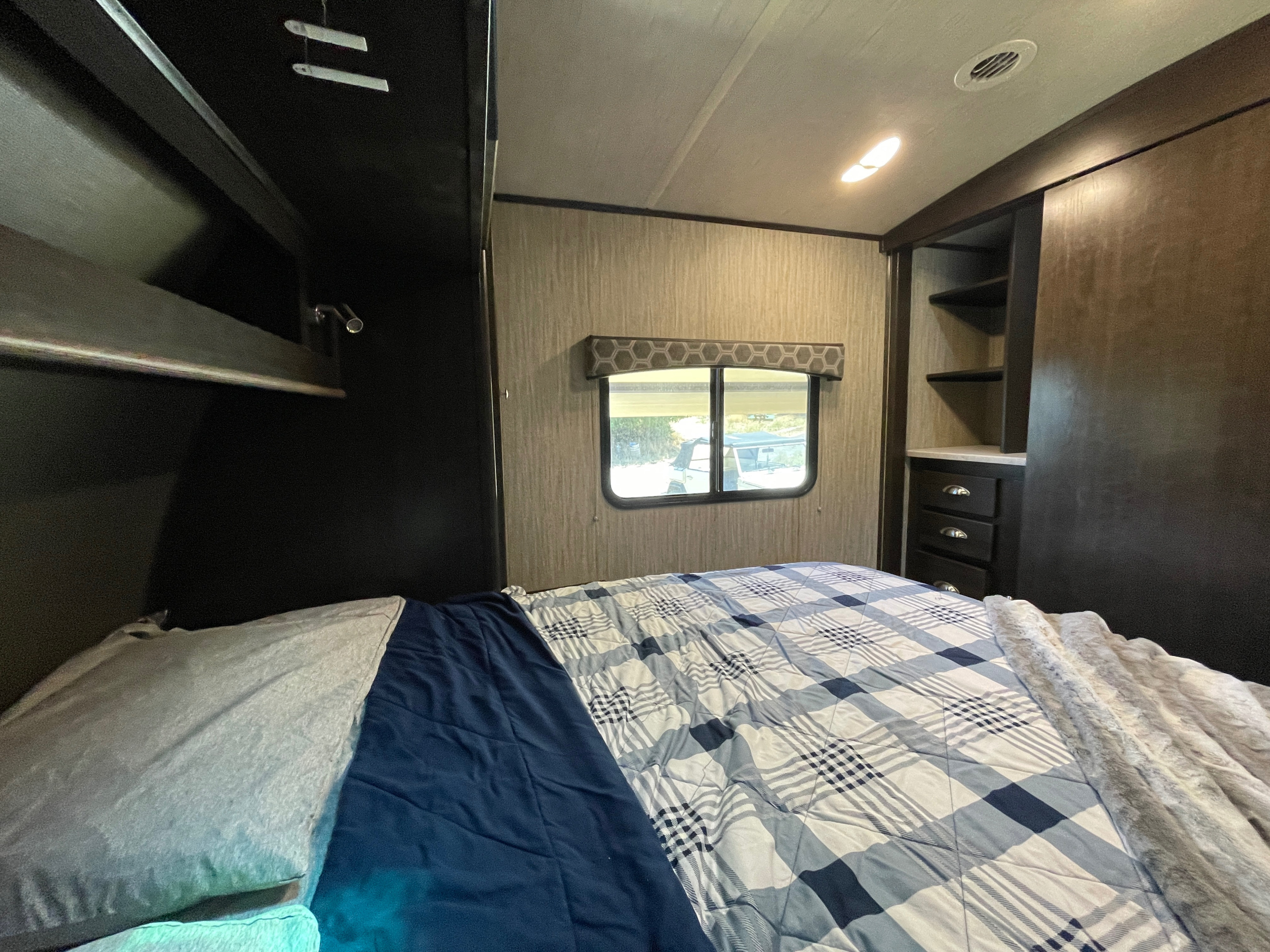 Cozy RV rental bedroom featuring a comfortable bed with plaid comforter, window view, and built-in storage.. Cruiser RV Shadow Cruiser 2019
