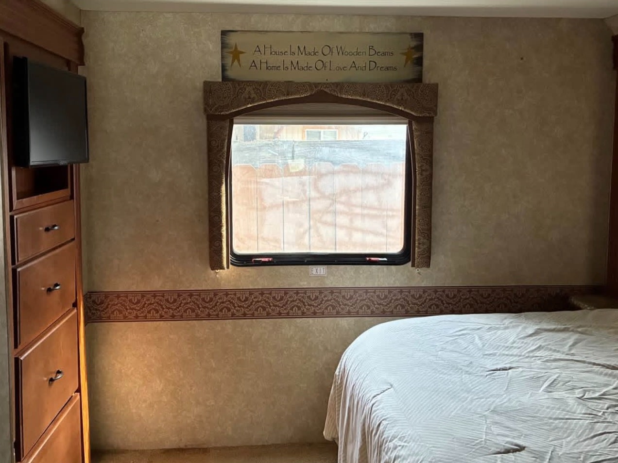 Cozy RV rental bedroom featuring a bed, window, wall-mounted TV, and a decorative sign, ideal for your travels.. Coachmen Thor Motor Coach 2009