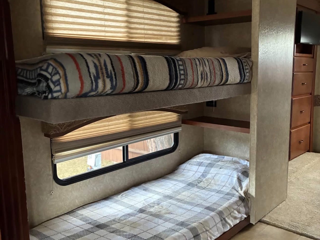 Cozy rv rental bunk beds with window and storage. Features an upper bed with a striped blanket and a lower bed with a plaid cover.. Coachmen Thor Motor Coach 2009