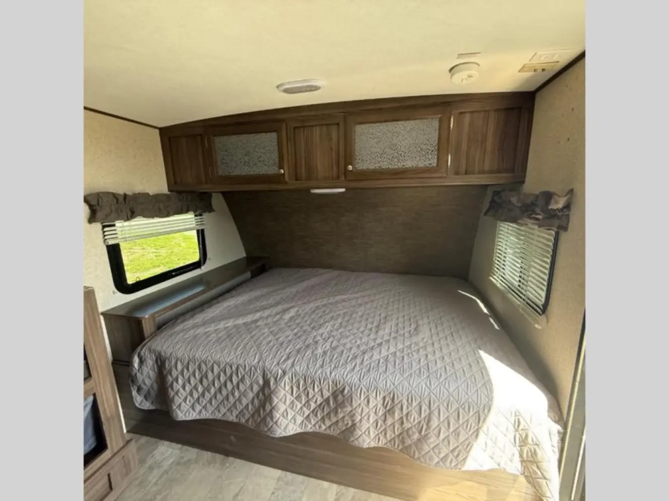 Interior of a comfortable RV rental bedroom, featuring a large bed, overhead cabinets, and bright windows for a relaxing journey.. Coachmen Apex Nano 2018