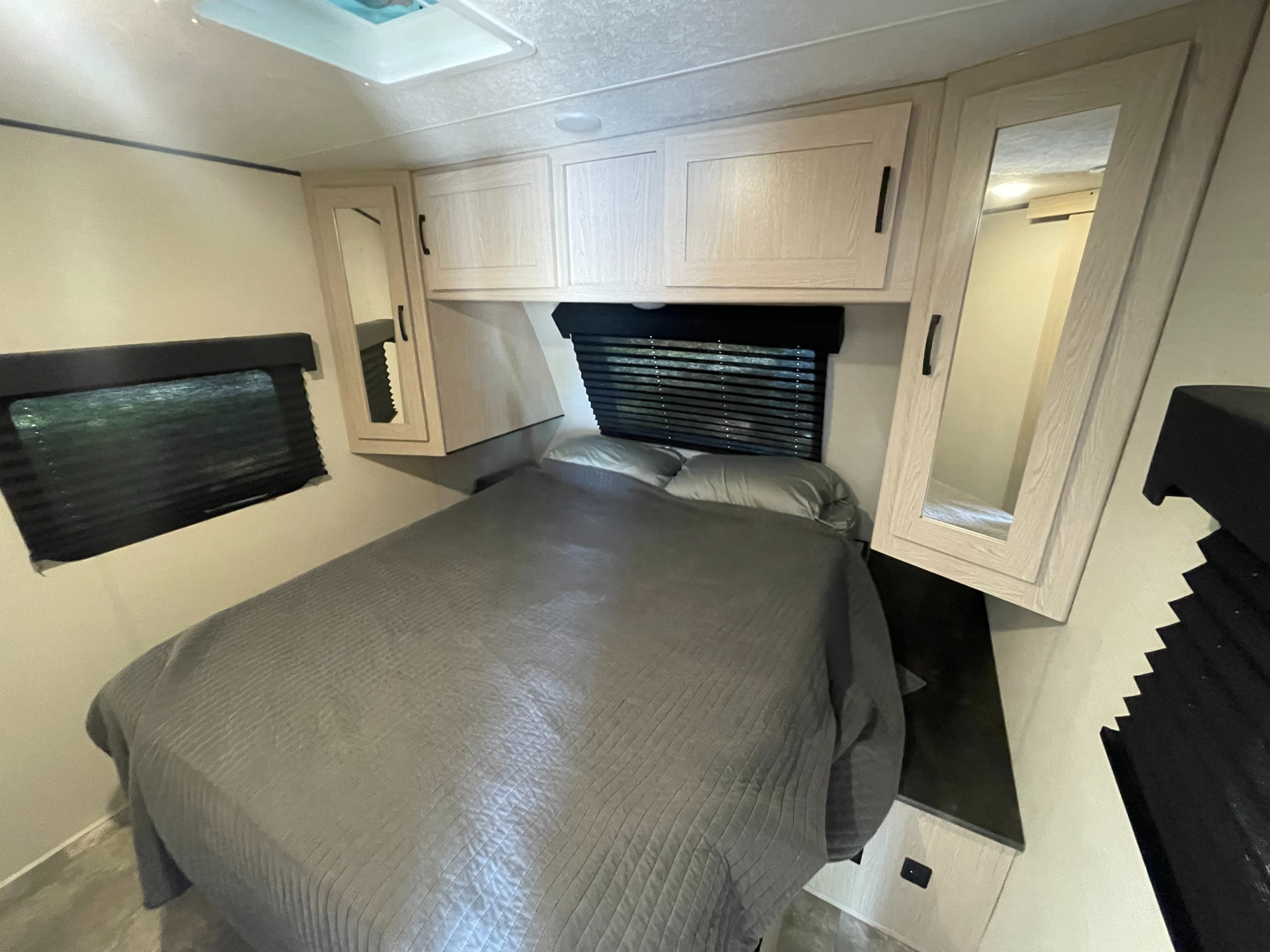 Experience comfort in this RV rental bedroom featuring a cozy bed, overhead cabinets, and windows with blinds.. Coachmen Apex 2022