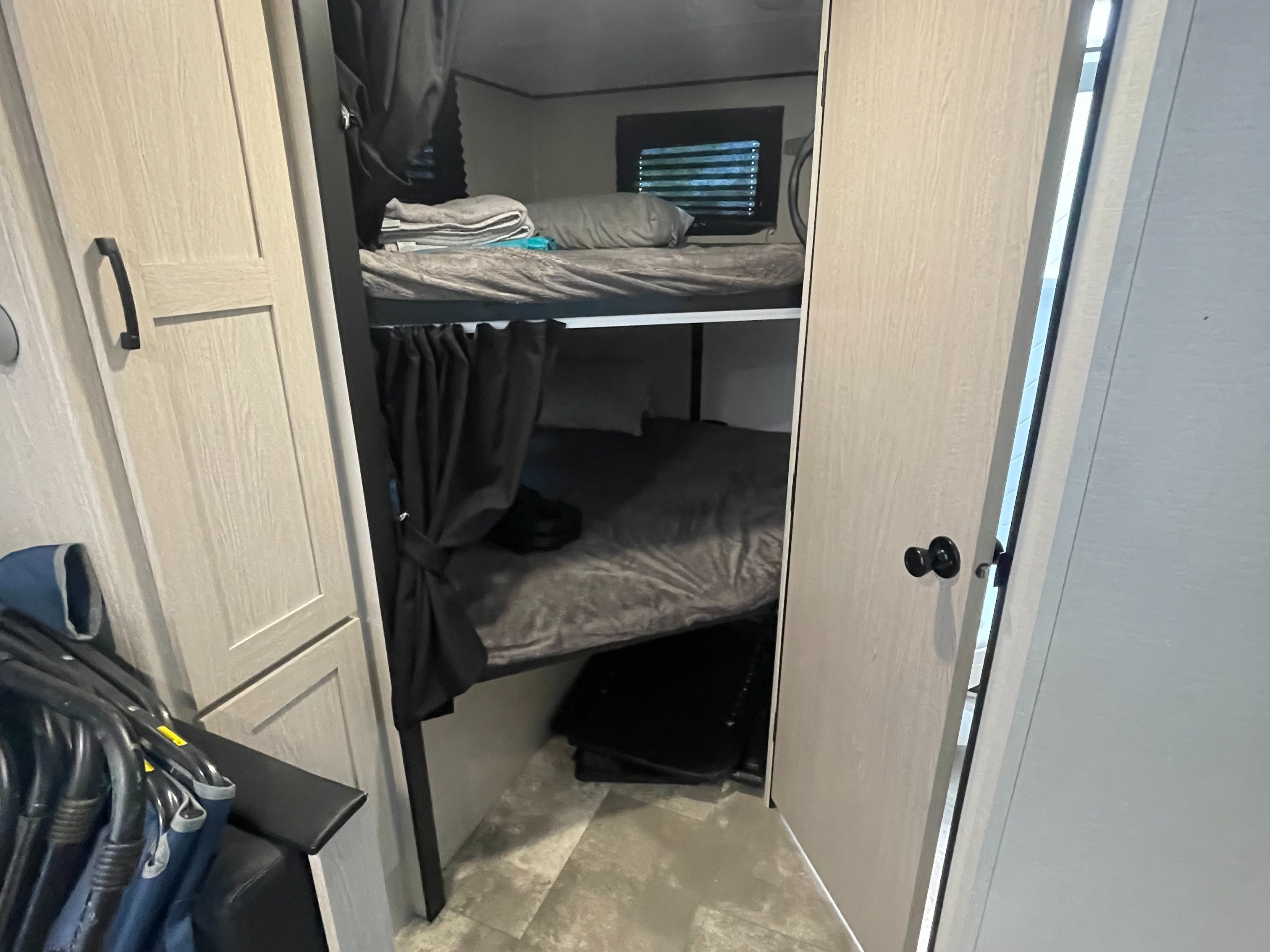 View of cozy bunk beds in an **rv rental**, featuring gray bedding, privacy curtains, and nearby cabinetry for storage.. Coachmen Apex 2022