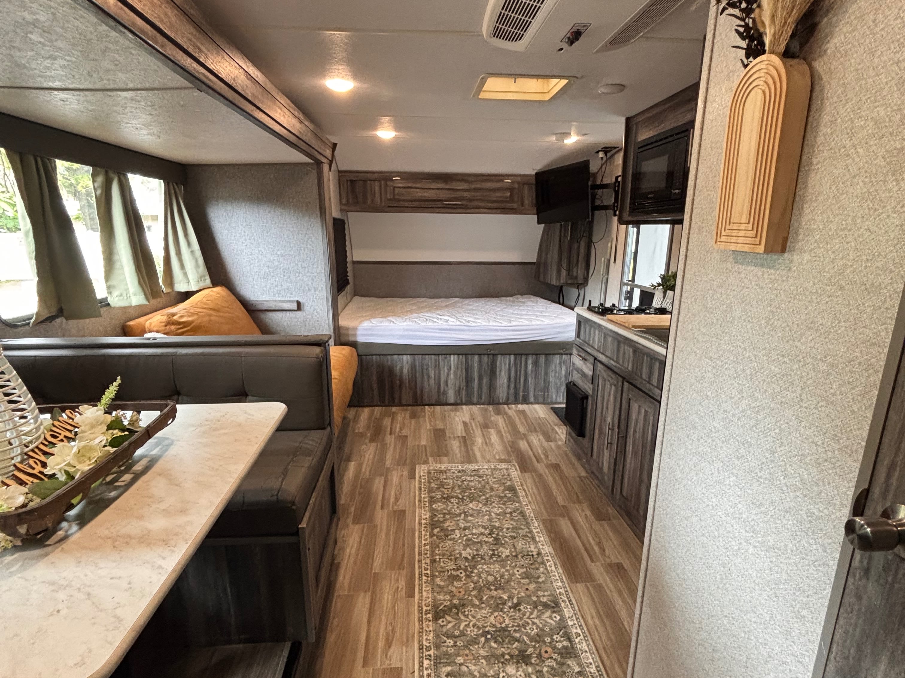 Cozy RV rental interior with dining booth, bedroom, and kitchen. Features wood-look flooring and modern decor for comfortable travel.. Forest River Wildwood FSX 2019