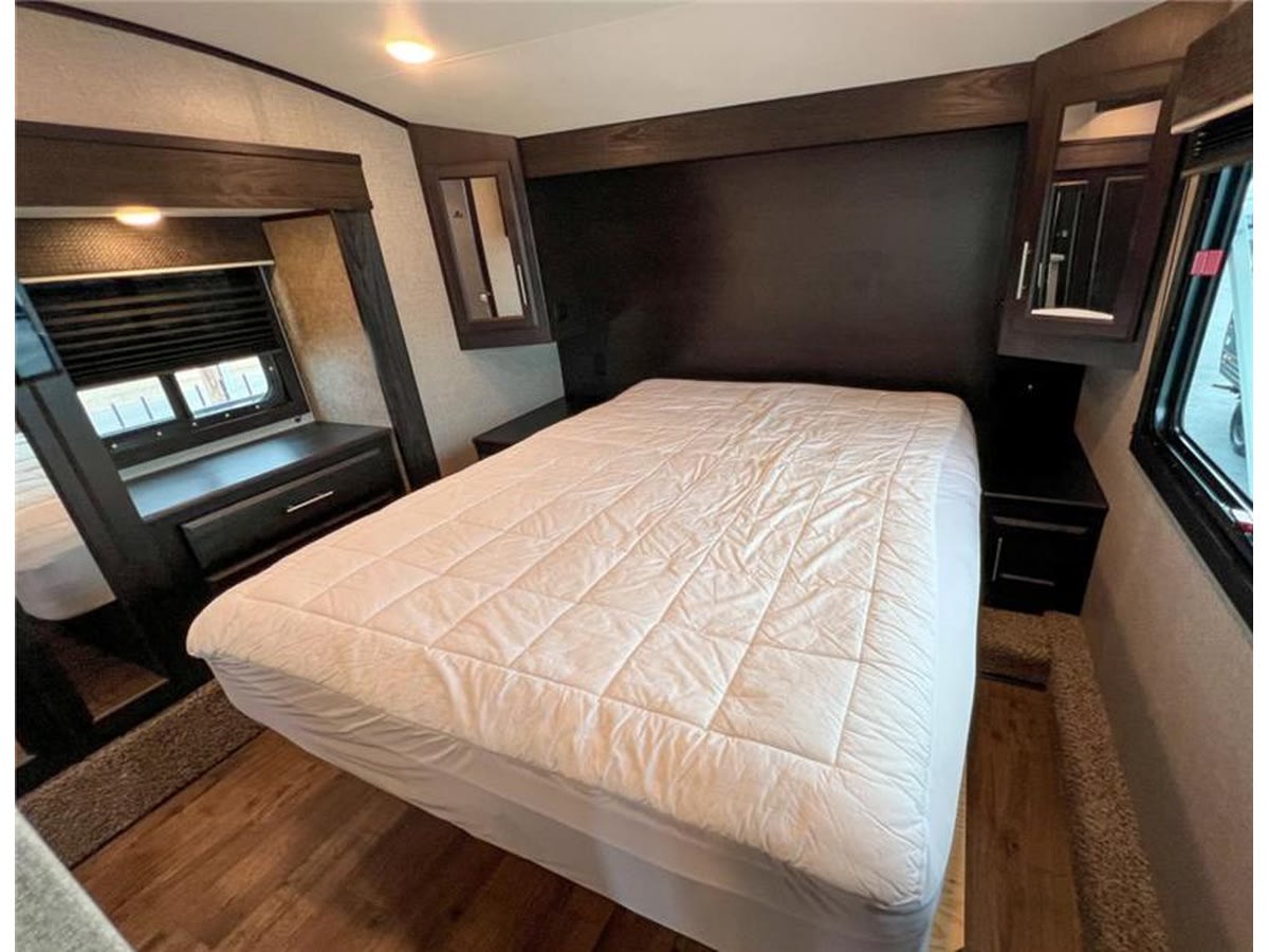 Cozy RV rental bedroom featuring a large bed, built-in storage, and windows. Ready for a comfortable travel experience.. Jayco Eagle HT 2021