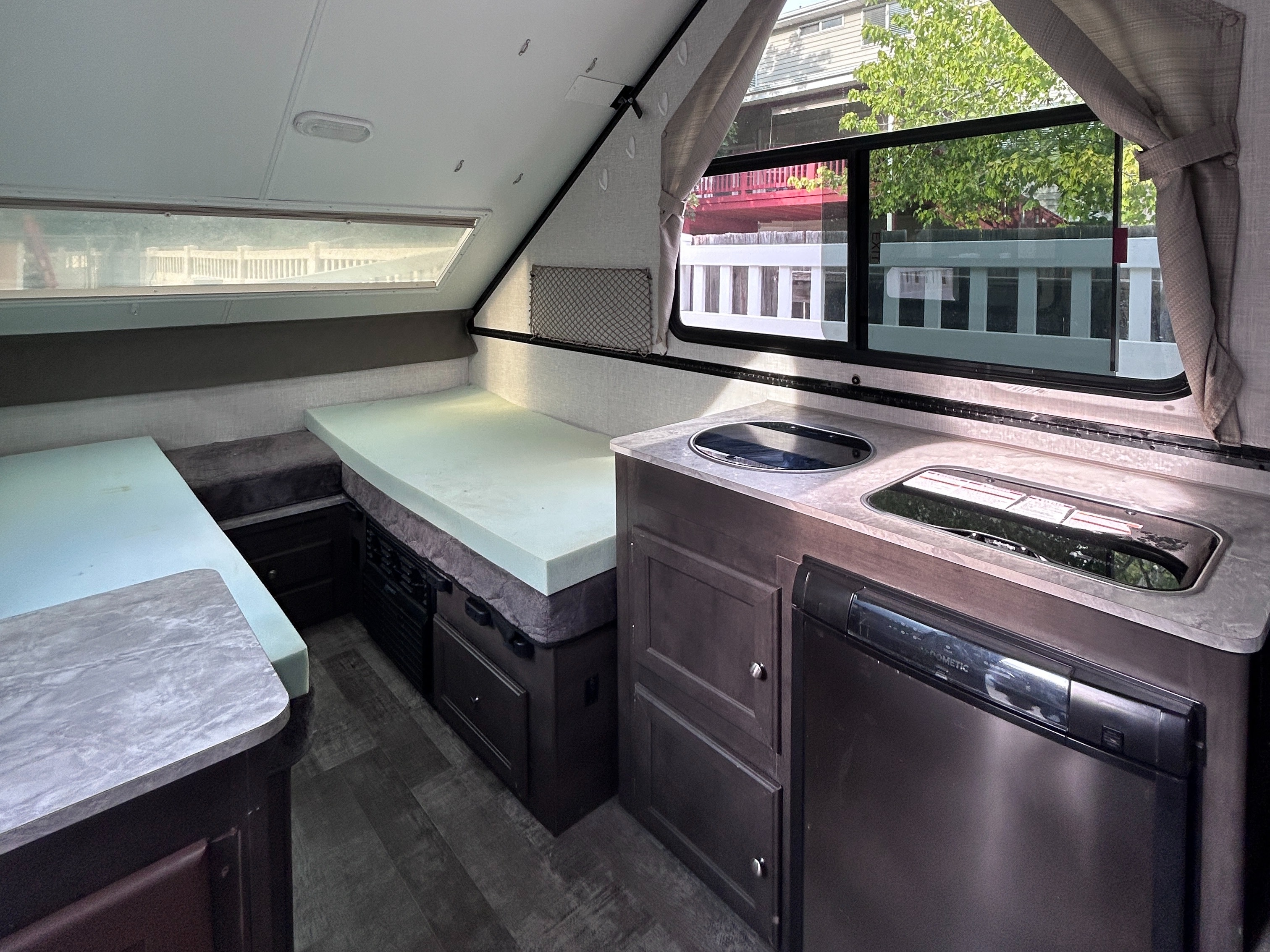 Interior of an RV rental showing a compact kitchen with Dometic fridge, sink, and two beds with light green foam toppers.. Forest River Rockwood Premier 2021