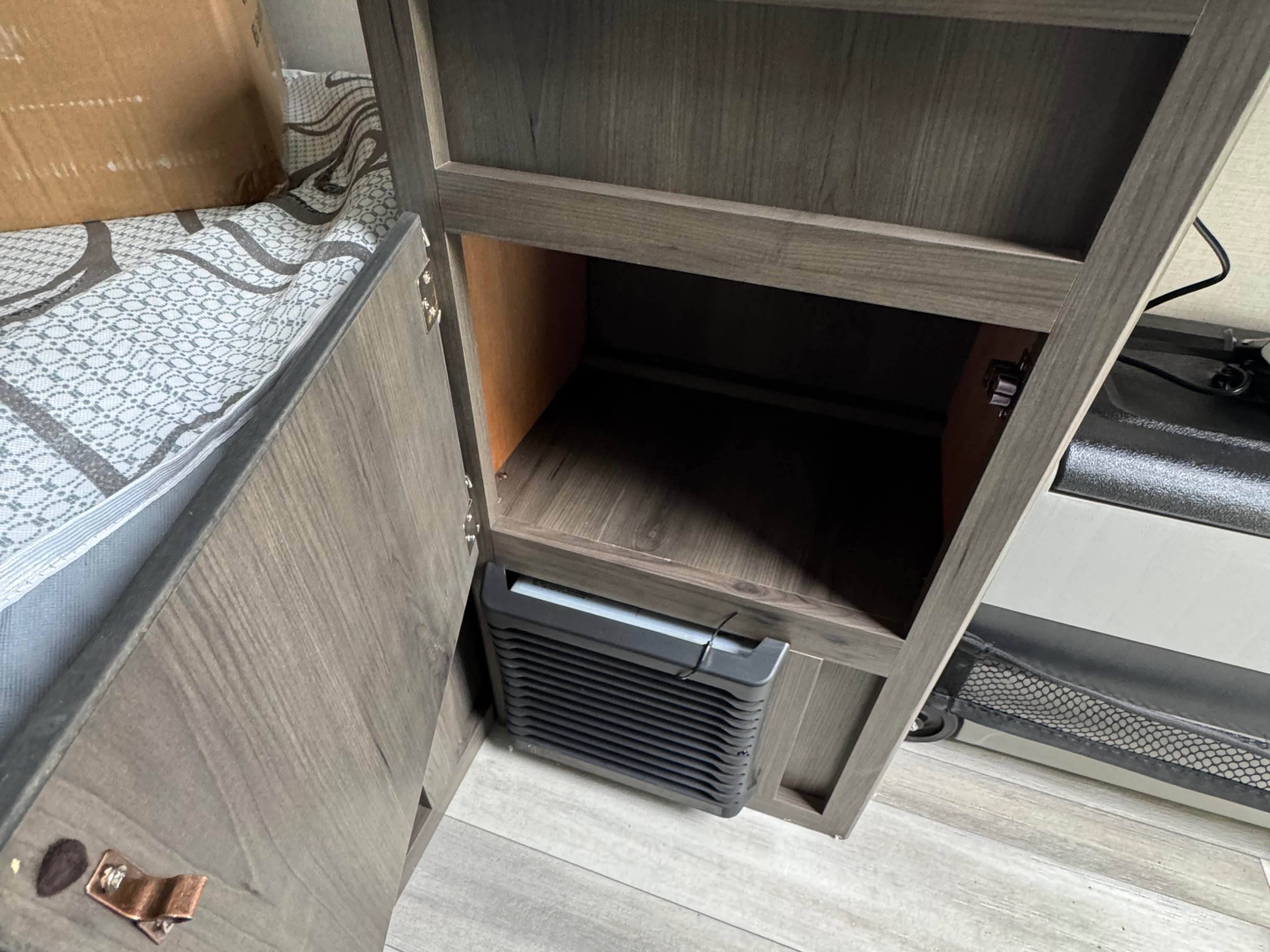 RV rental interior: open cabinet with lower vent unit, upper storage shelf. Adjacent bed with patterned sheet and box visible.. Forest River Coachmen Clipper 2023