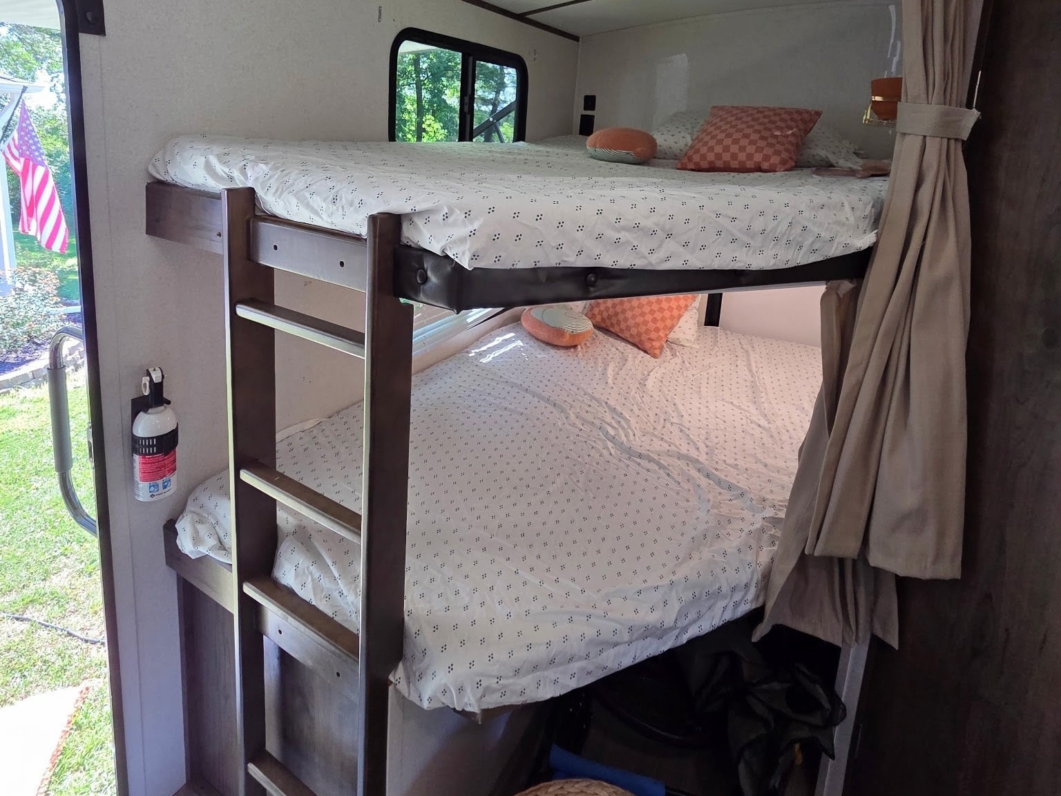 Cozy bunk beds inside an RV rental, featuring patterned sheets, a window with an outdoor view, and a fire extinguisher.. Keystone RV Passport Grand Touring 2020