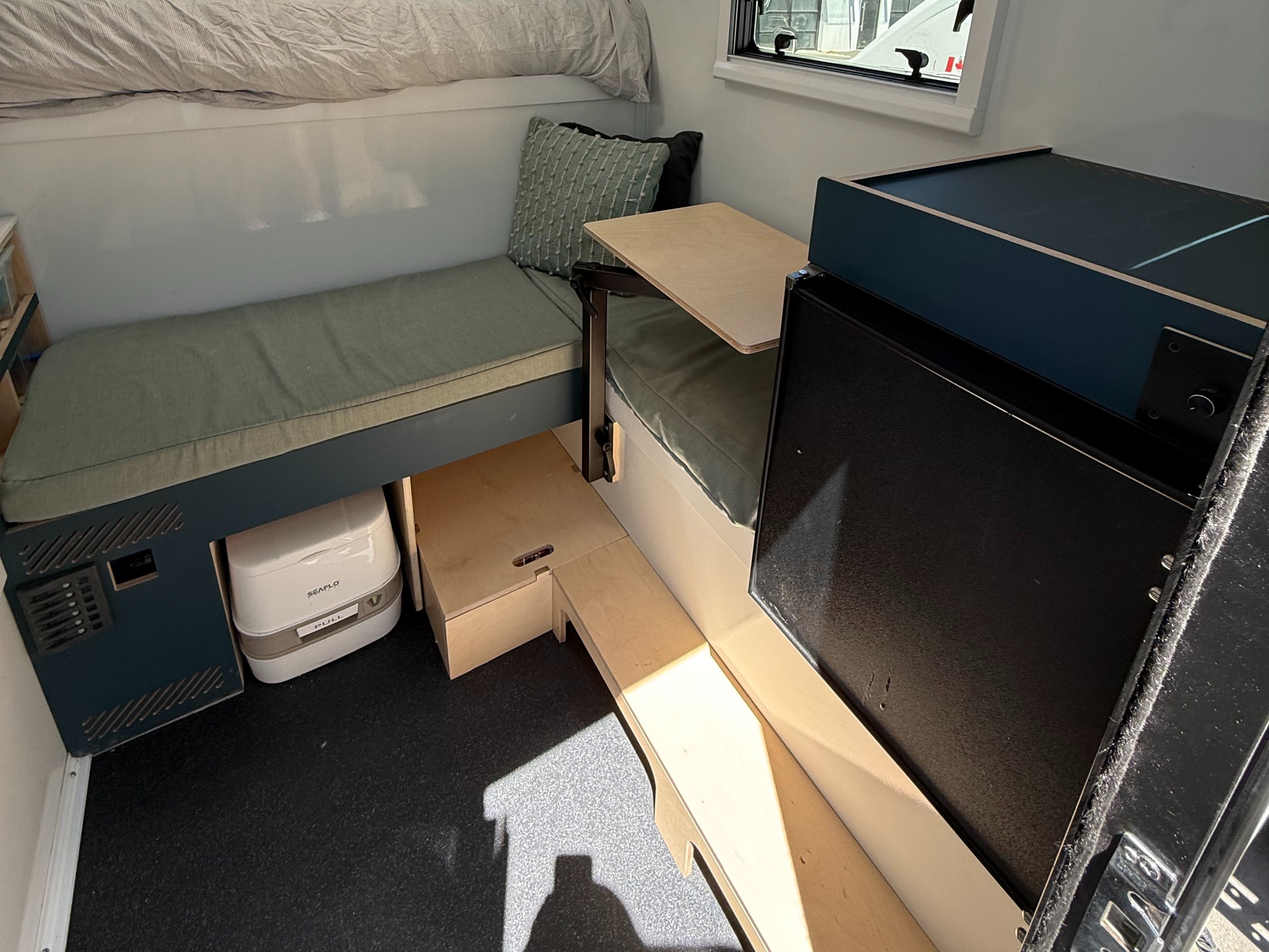 Compact RV rental interior with a bunk bed, sage green seating, portable toilet, and clever storage solutions.. Custom Camper 2025