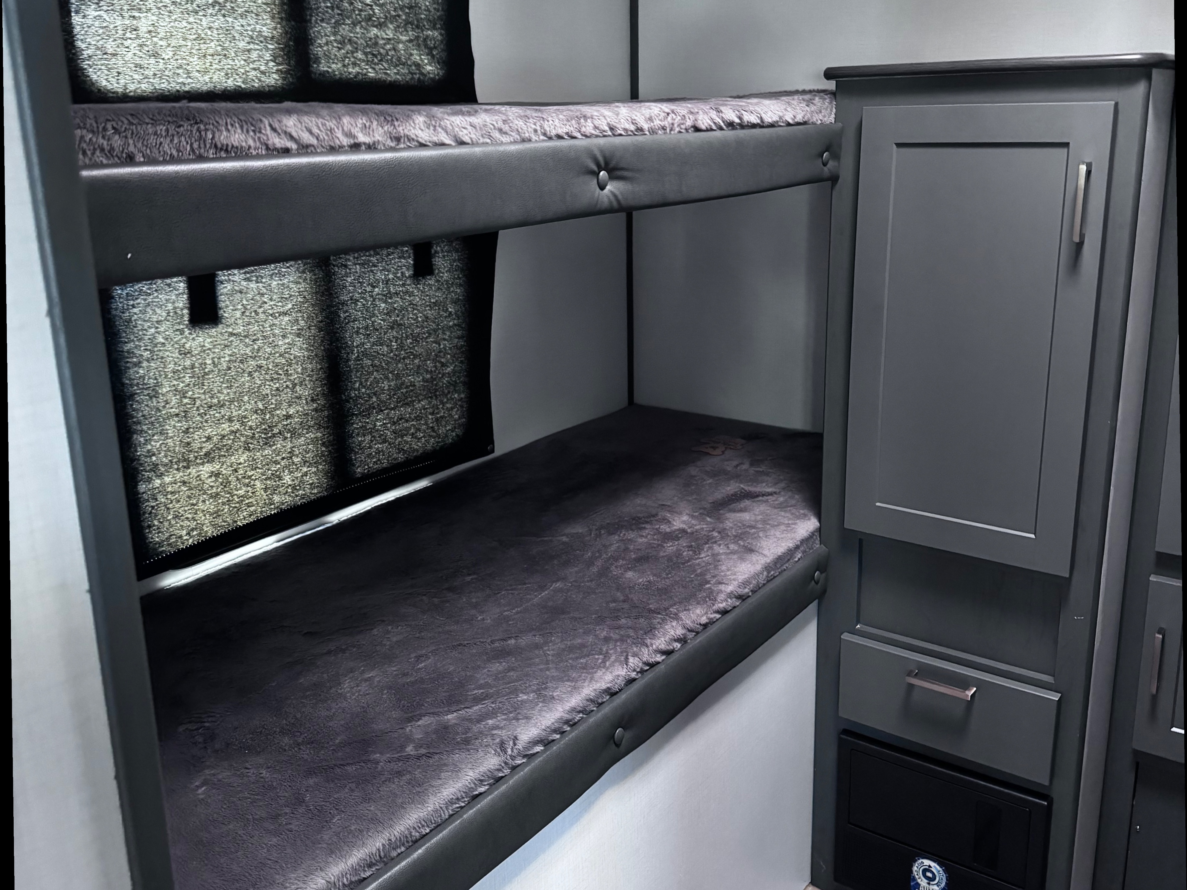Interior view of an rv rental featuring cozy bunk beds with dark gray mattresses and an adjacent storage cabinet.. Keystone RV Bullet Ultra Lite 2022