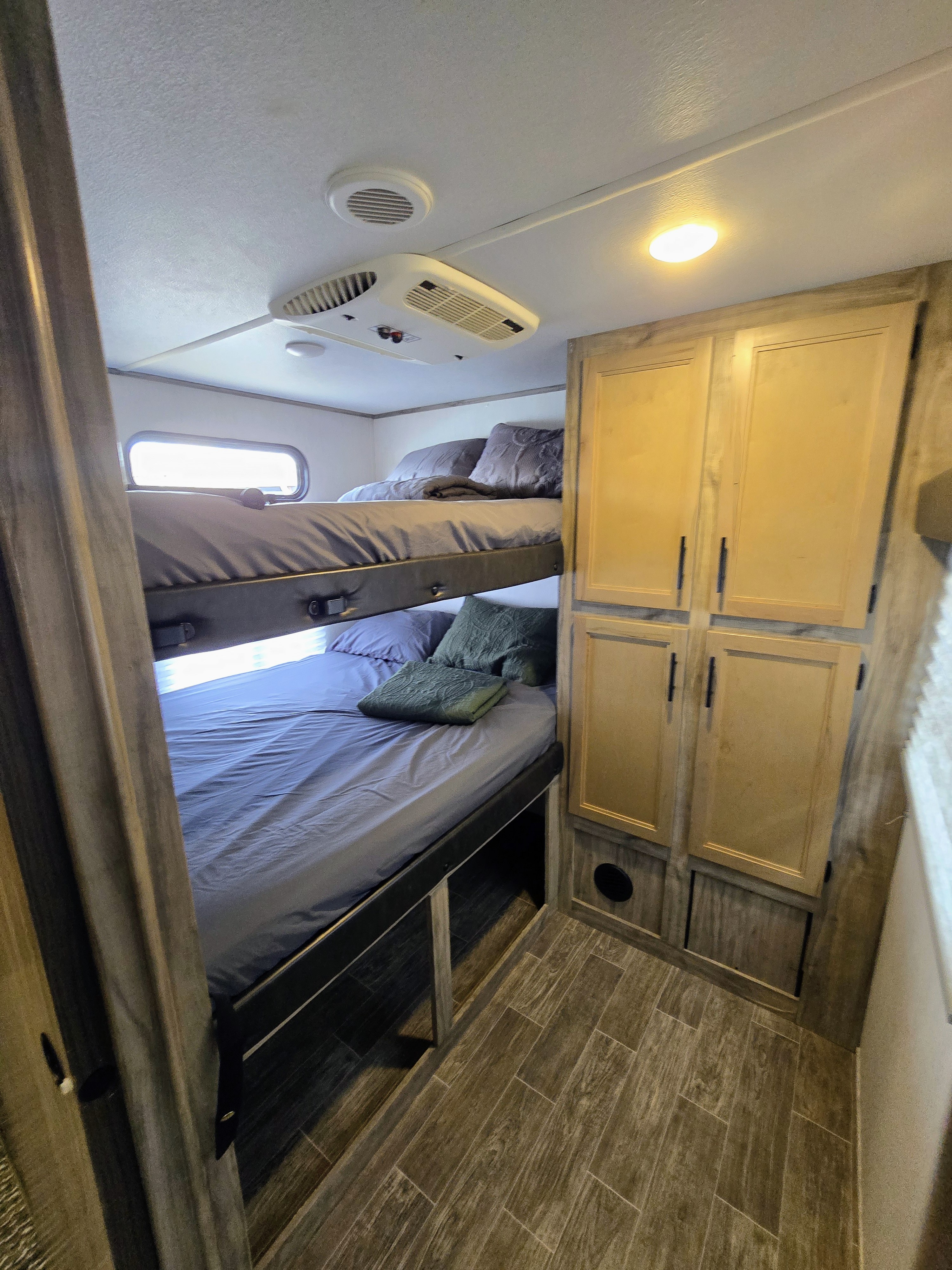 Inside this **rv rental**, dual bunk beds are ready with bedding. A ceiling AC unit and wooden storage cabinets are also visible.. Forest River Alpha Wolf 2021