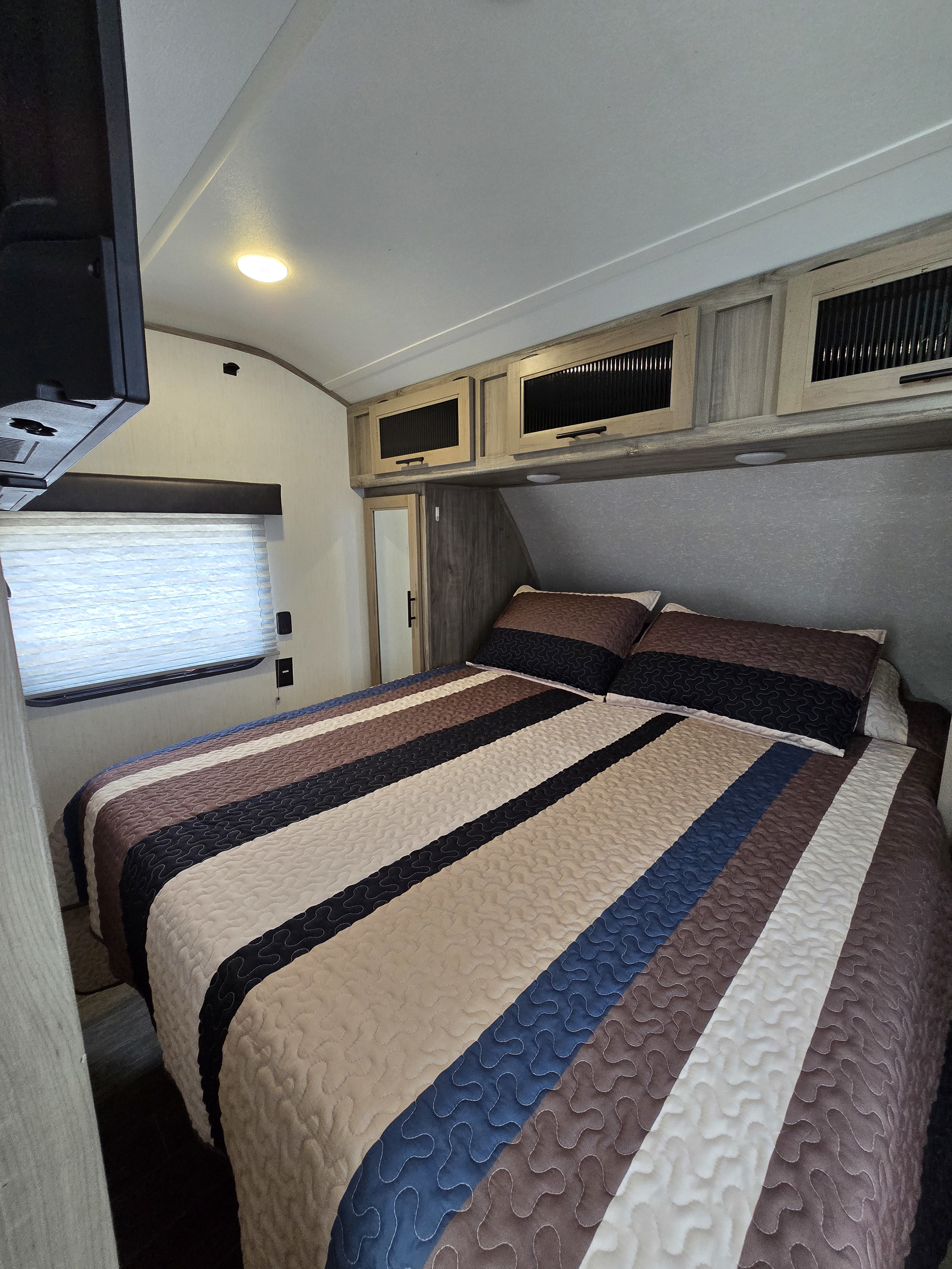 Cozy RV rental bedroom with a vibrant striped quilt, overhead storage, a large window, and TV for your travels.. Forest River Alpha Wolf 2021