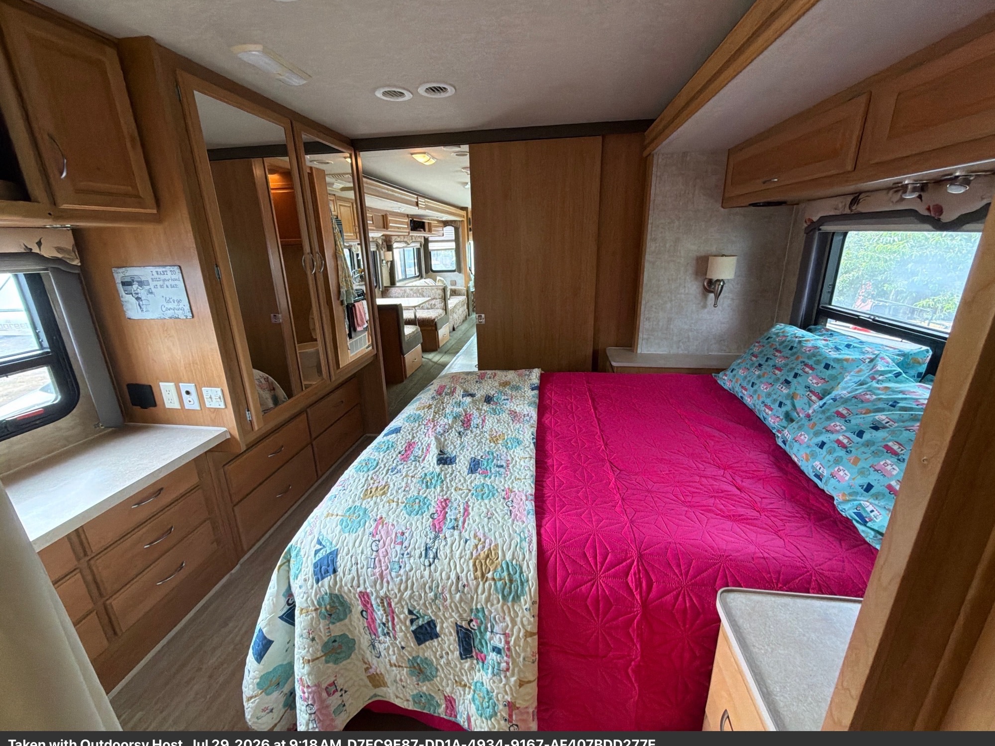 Cozy RV rental bedroom featuring a comfy bed with pink & patterned bedding, ample storage, and a view into the living area.. Fleetwood Bounder 2008