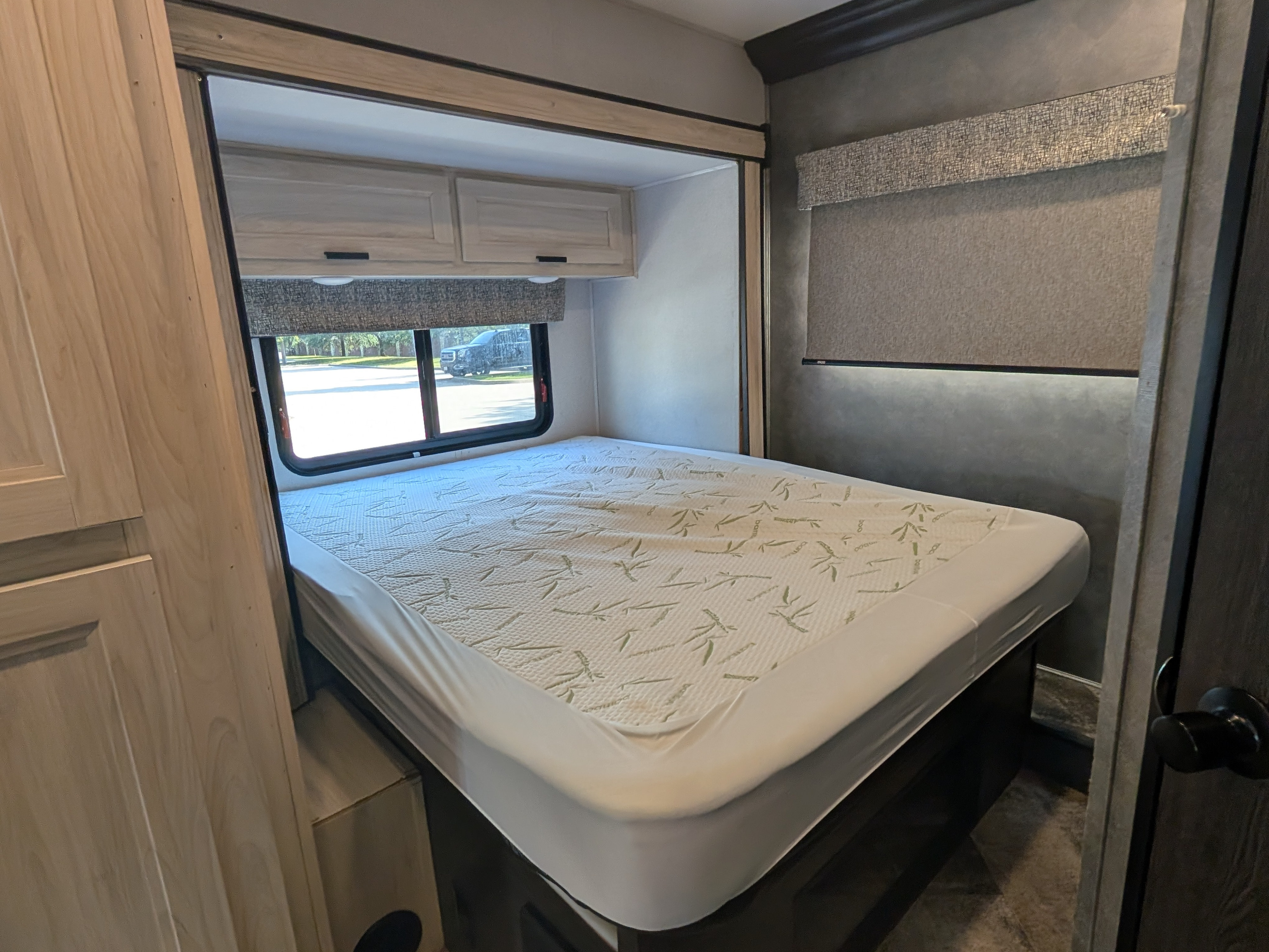 Cozy RV rental bedroom featuring a bed with bamboo pattern mattress protector, overhead cabinets, and a window with a view.. Forester LE 2021