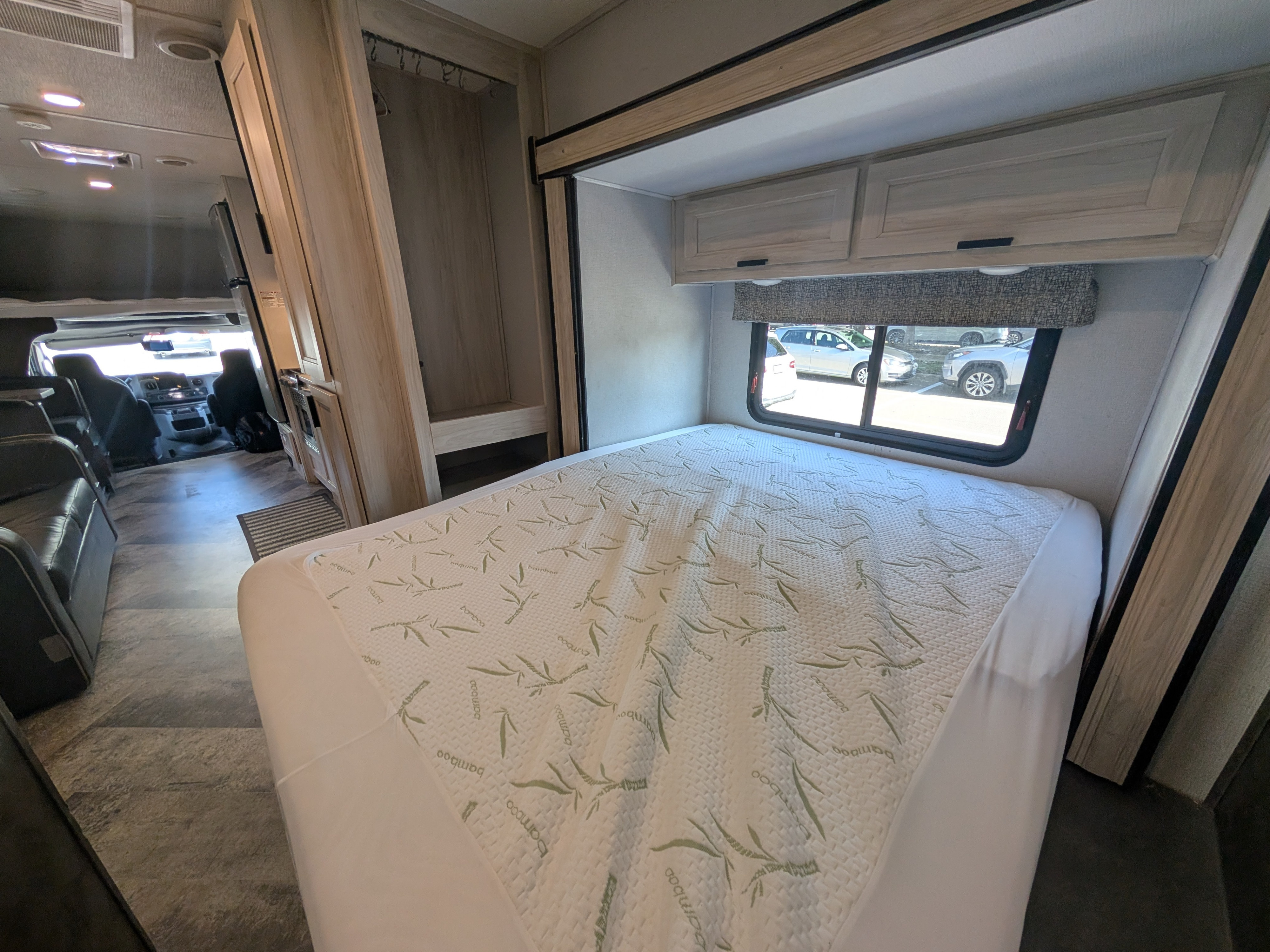 This RV rental interior showcases a cozy bedroom with a patterned bamboo mattress, overhead cabinets, and a window view, offering comfort and convenience.. Forester LE 2021
