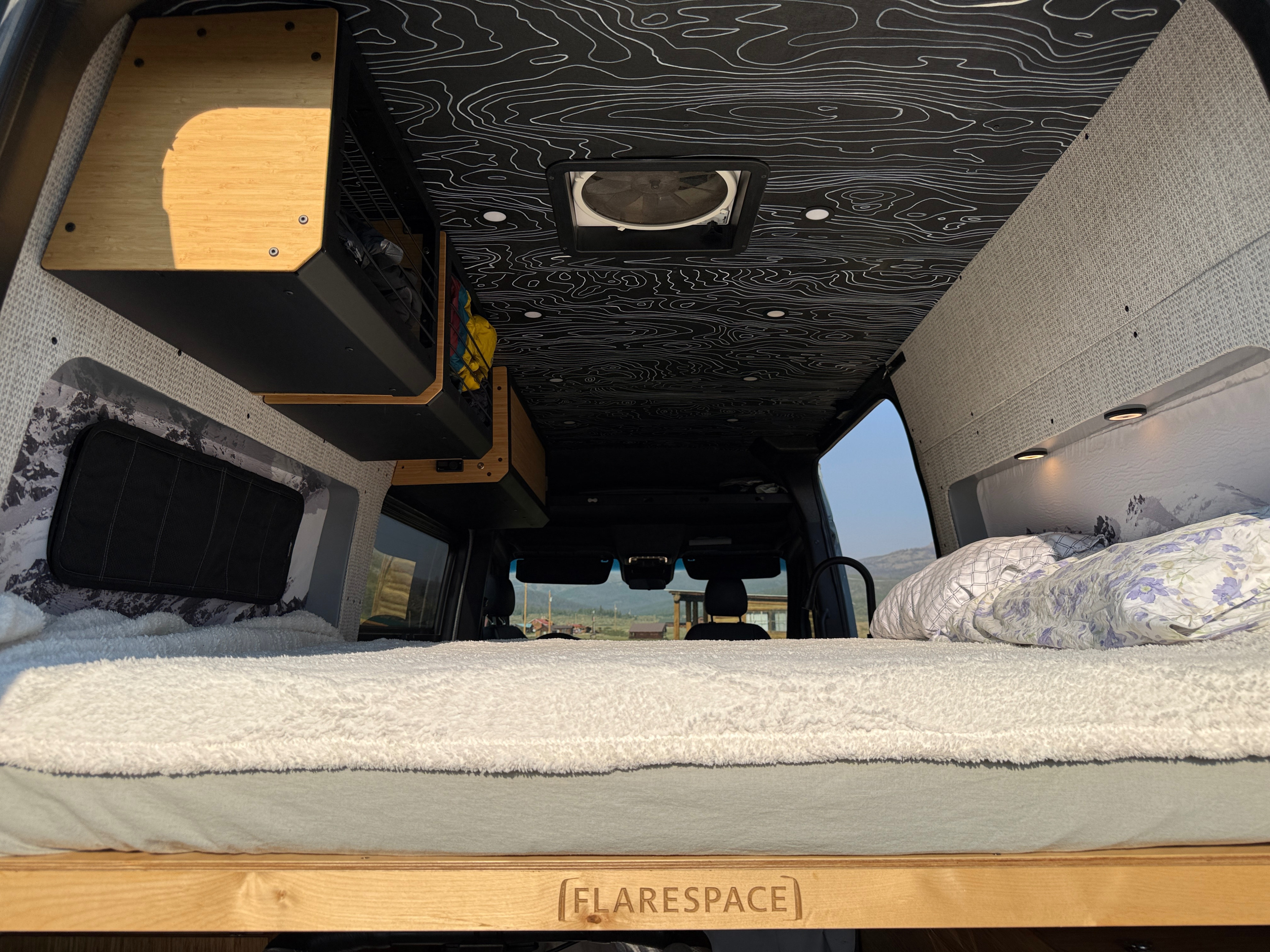 Cozy RV rental interior with a comfortable bed, custom overhead storage, and a distinctive topographical map ceiling design.. Mercedes-Benz Sprinter 2021