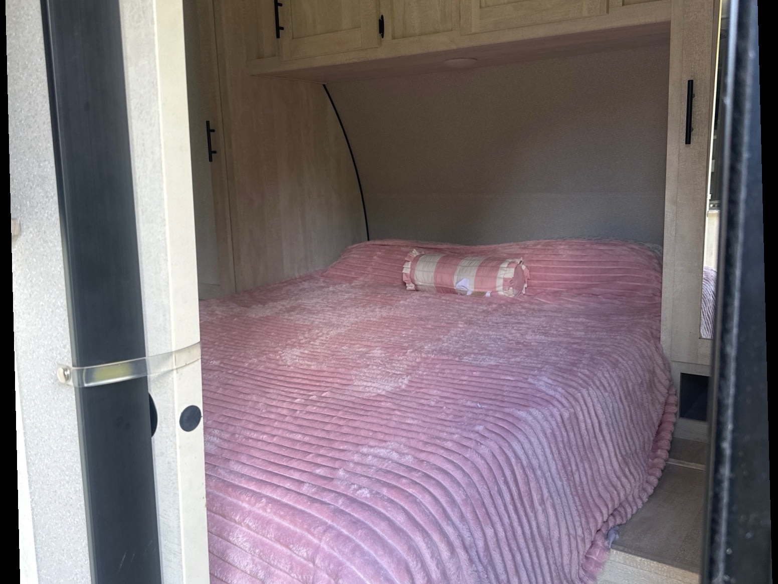 Inviting RV rental bedroom with a soft pink bed, striped bolster pillow, and overhead storage cabinets.. Forest River Shasta 2022