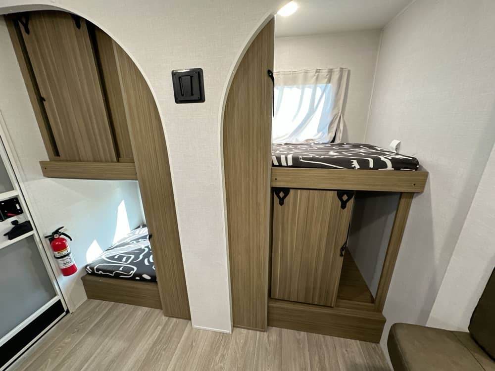RV rental interior featuring cozy bunk beds, storage, and safety equipment like a fire extinguisher, perfect for adventurers.. Forest River Wildwood FSX 2026
