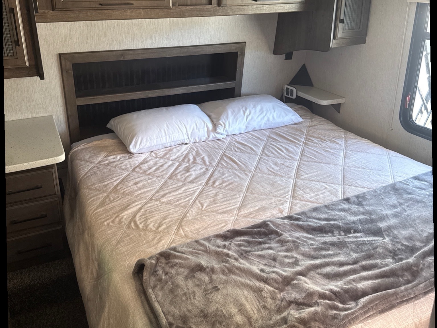 Cozy RV rental bedroom featuring a bed with white pillows, a quilted comforter, shelving headboard, and bedside storage.. Heartland Cyclone 2018
