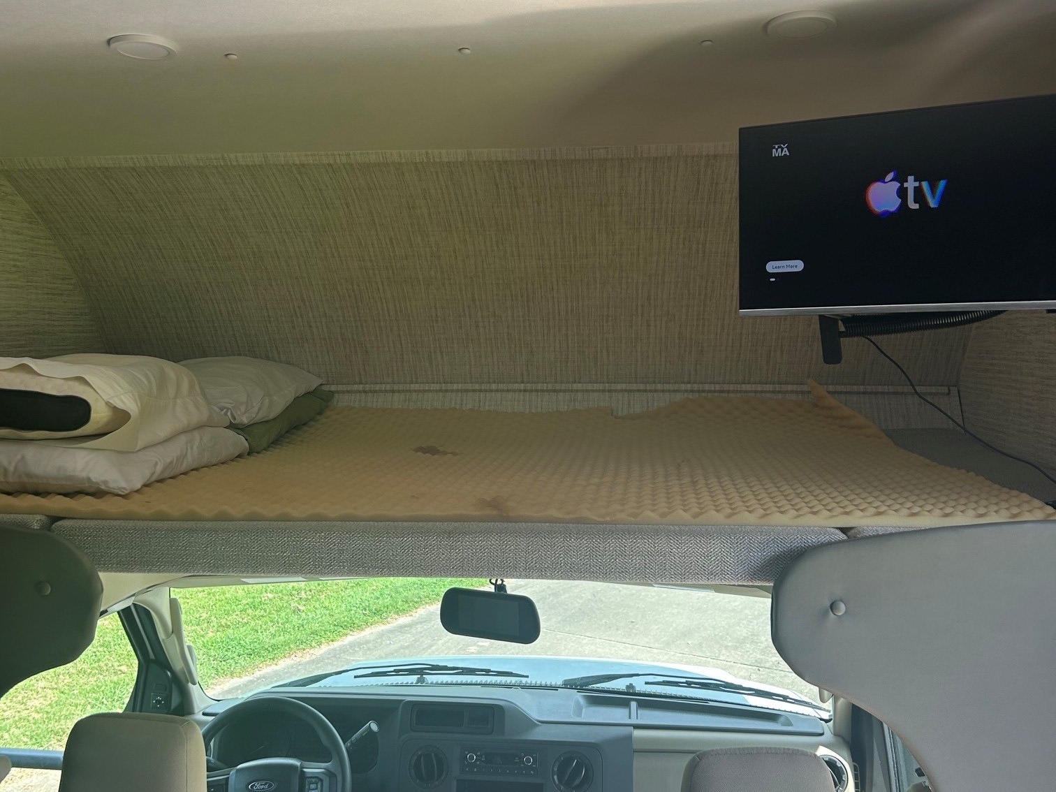 View inside this RV rental: a cozy overhead bunk bed with pillows, a mattress topper, and a mounted Apple TV for guests.. Jayco Redhawk SE 2025