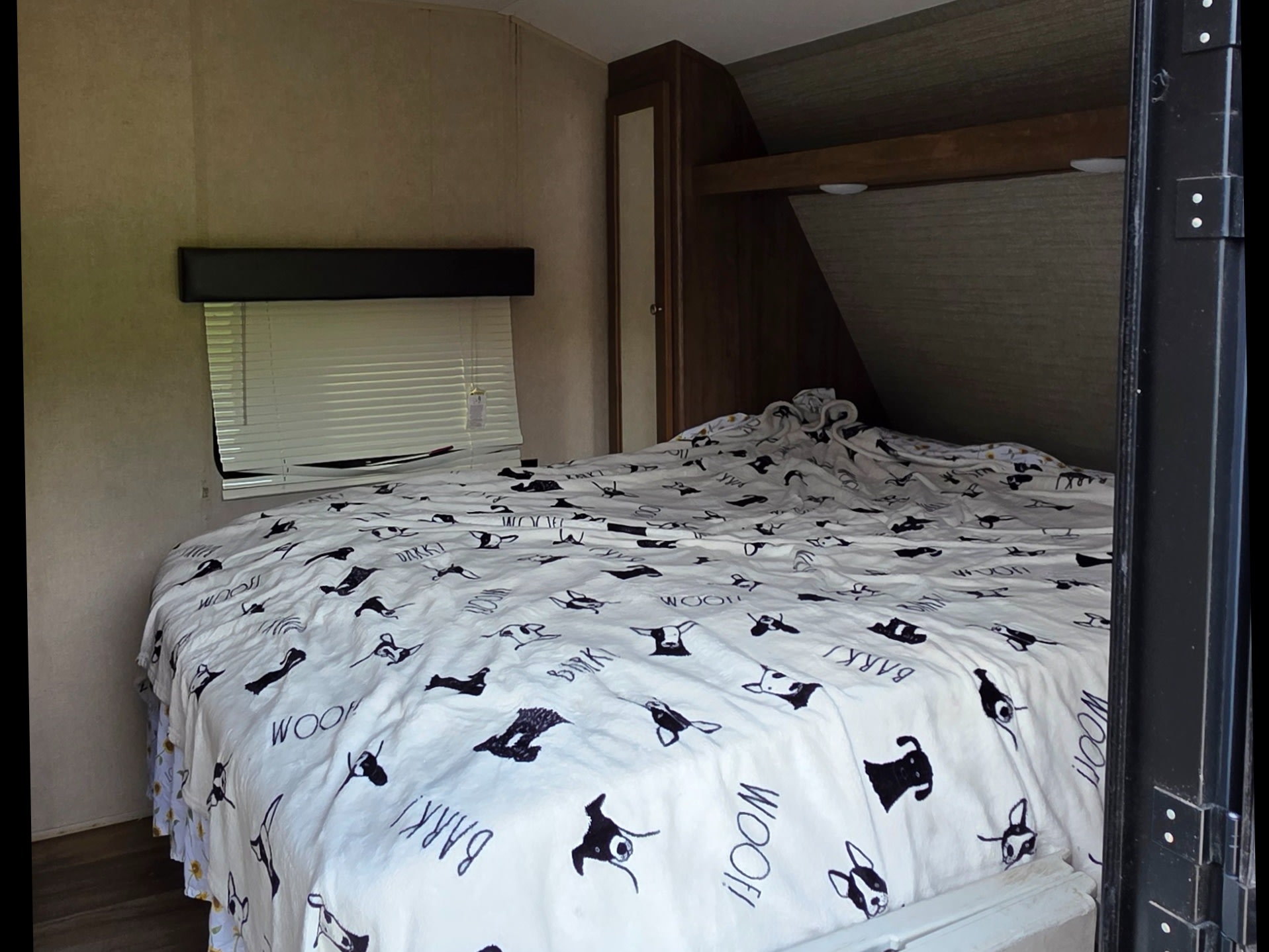 Cozy RV rental bedroom with a bed featuring fun dog-themed bedding, a window, and built-in storage. Ideal for travel adventures.. Dutchmen Aspen trail 2018