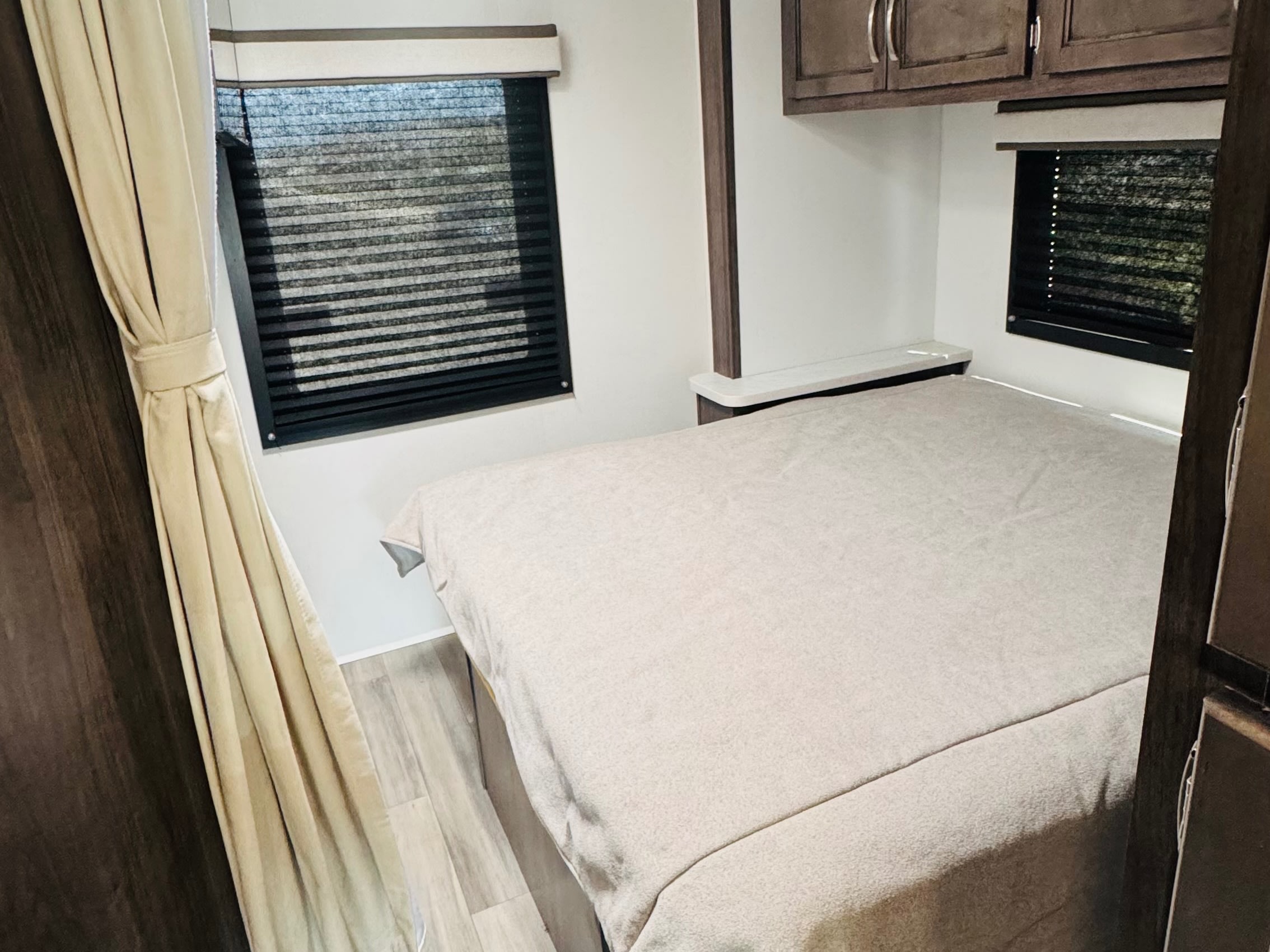 Interior view of an RV rental bedroom with a neatly made bed, windows with privacy blinds, and overhead cabinets.. ENTEGRA ODYSSEY 22C 2026