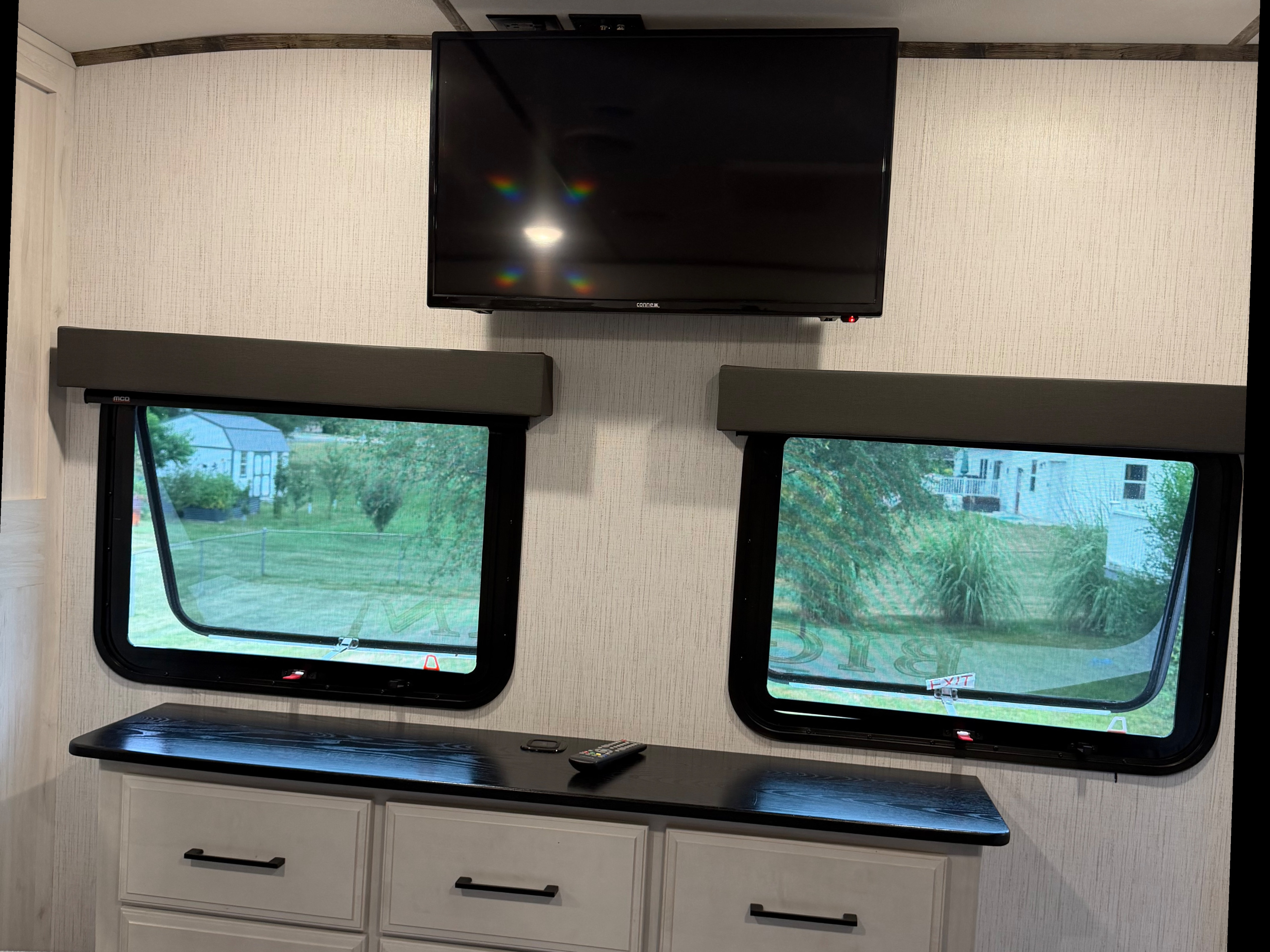 Mounted TV and two windows revealing an outdoor scene in a comfortable RV rental interior with drawer storage and a remote.. Heartland RVs Bighorn Traveler 2022