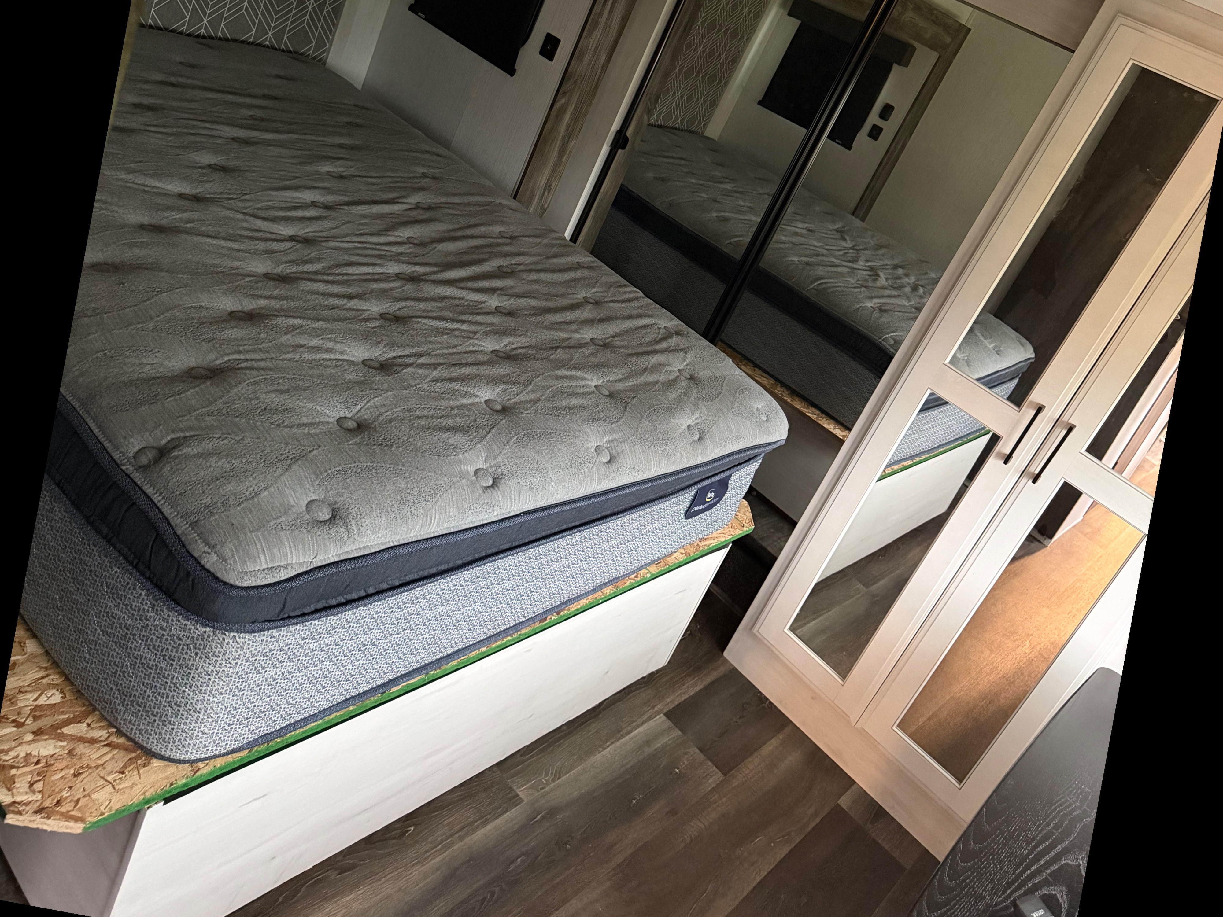 RV rental bedroom featuring a plush Serta mattress on a custom base, with mirrored closet doors and wood-look flooring.. Heartland RVs Bighorn Traveler 2022
