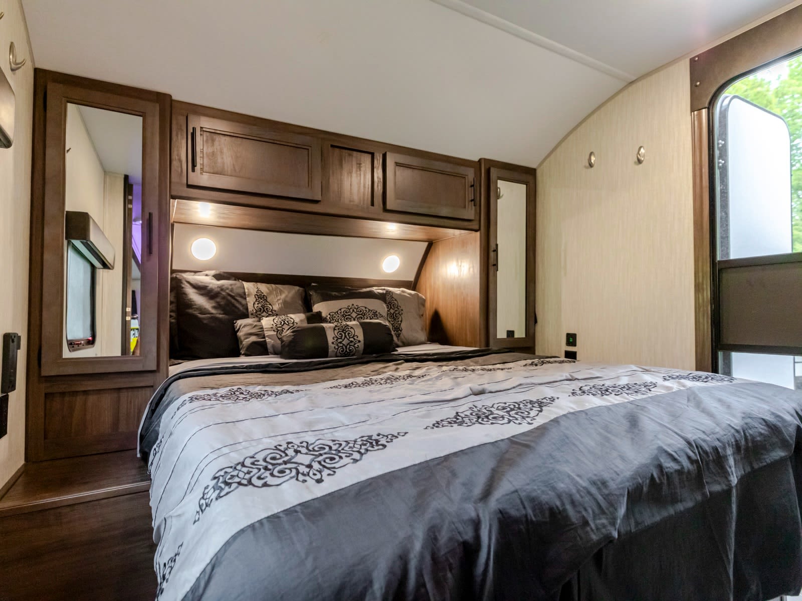 Cozy RV rental bedroom featuring a large bed with patterned gray bedding, built-in cabinets, and bright reading lights.. Forest River Cherokee 2020