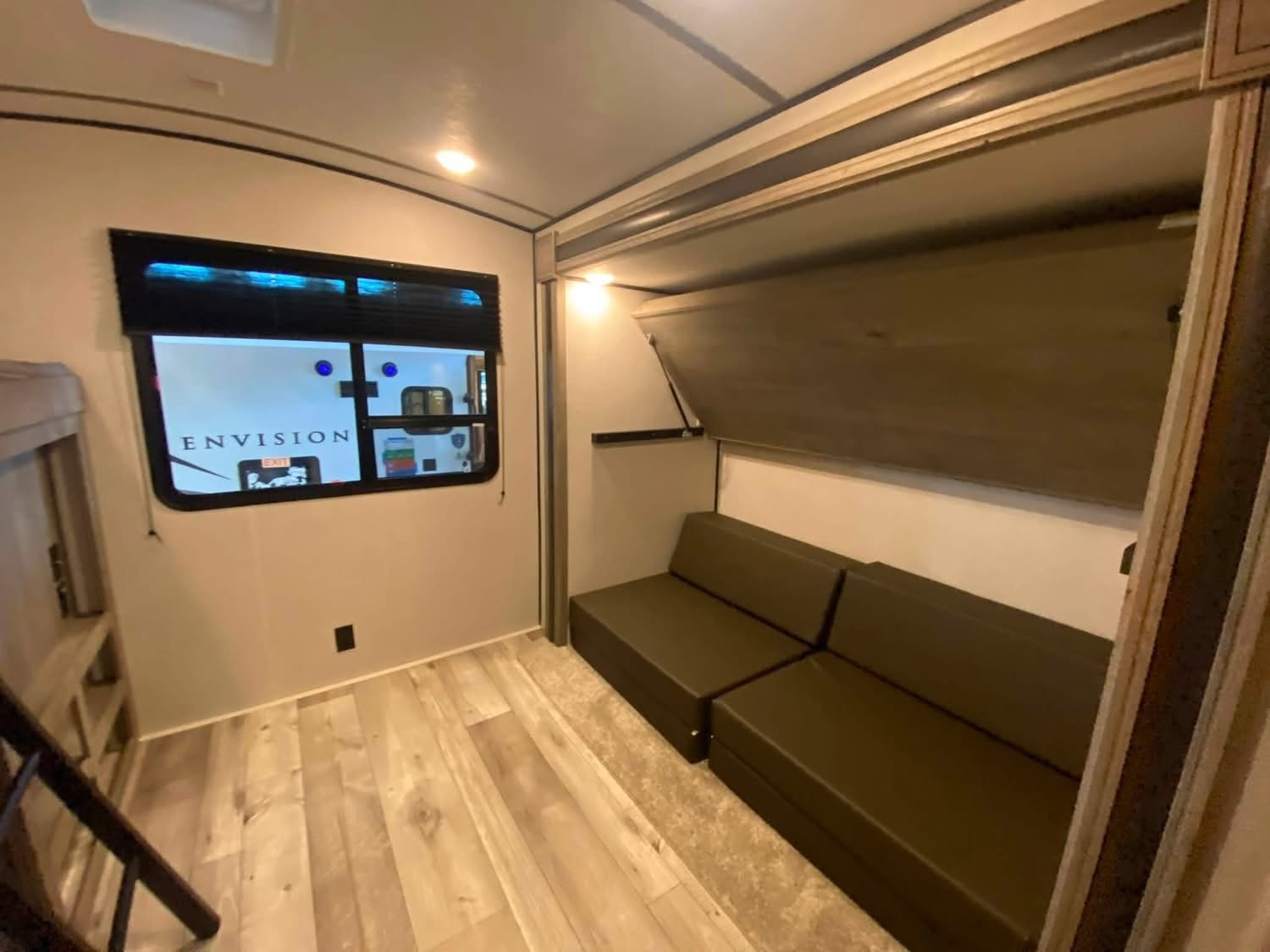 RV rental's cozy interior features a convertible sofa below a folded bunk, a window, and wood flooring. Ready for your trip.. Keystone RV Springdale 2021
