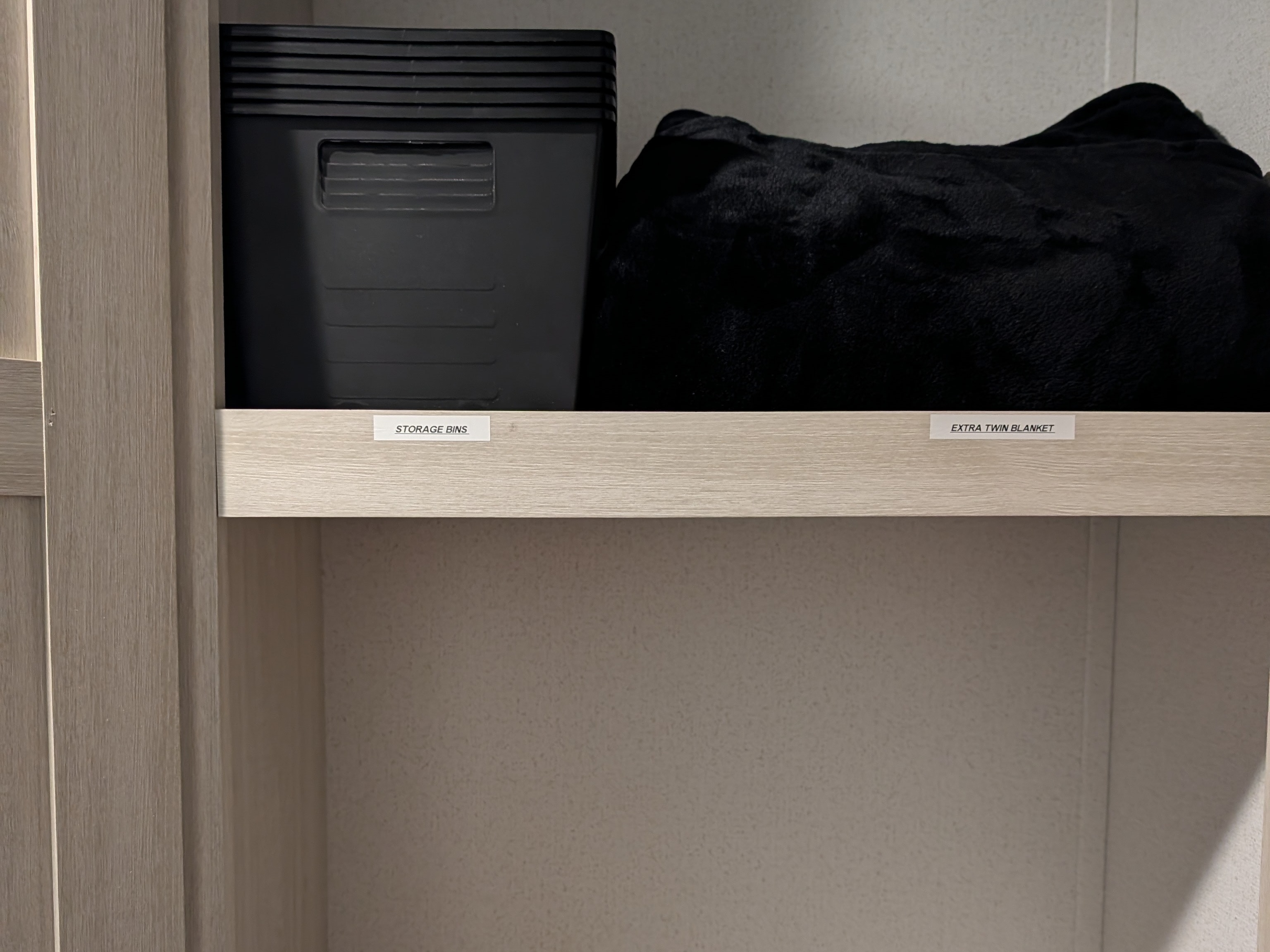 RV rental storage: Labeled shelf with a black storage bin and an extra twin blanket, neatly organized.. Forest River 303BHCE Camping 2026