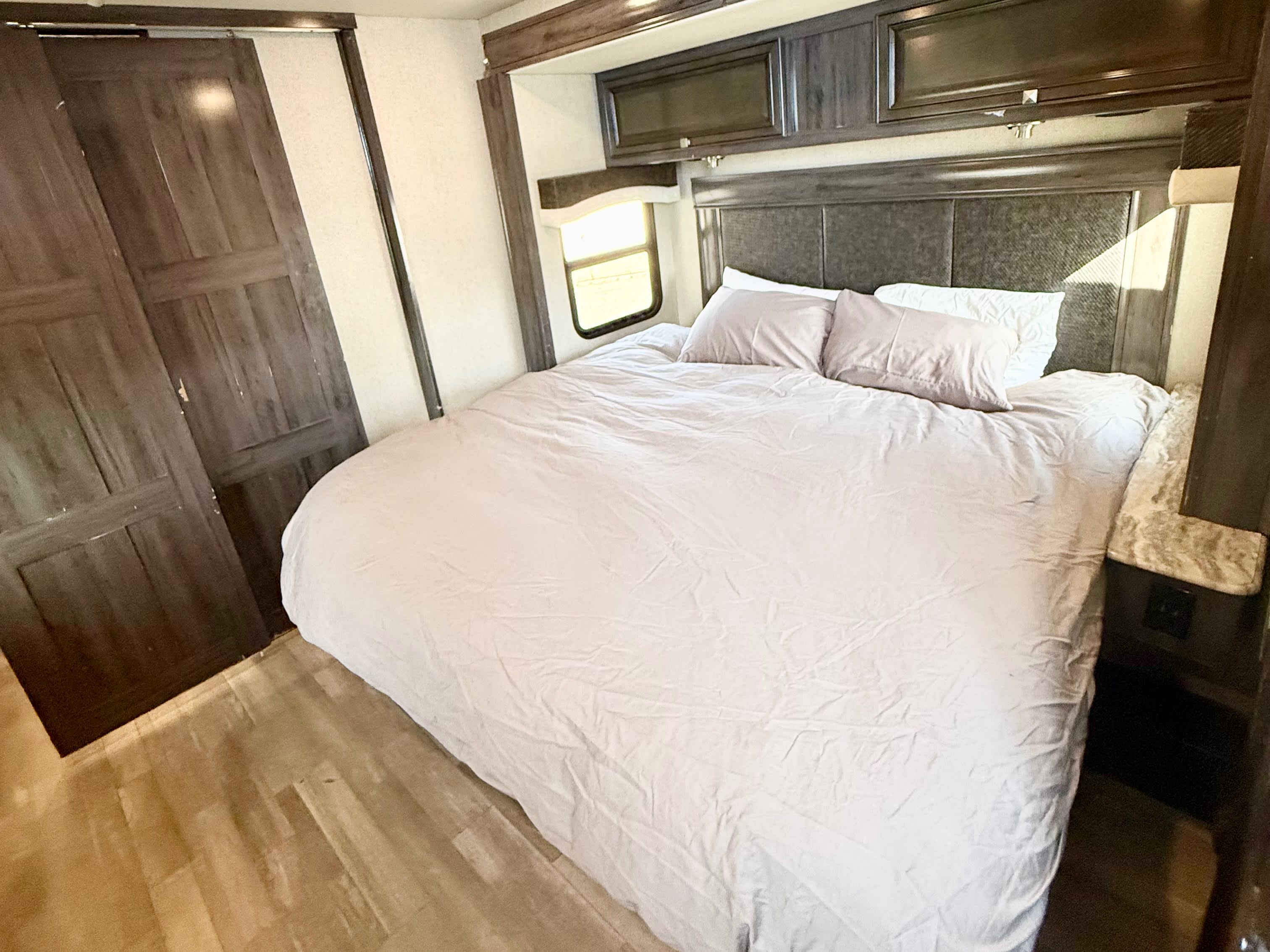Cozy rv rental bedroom with a large bed, dark wood cabinets, a side window, and light wood flooring.. Flair-Fleetwood Flair-Fleetwood Motorhome 2020