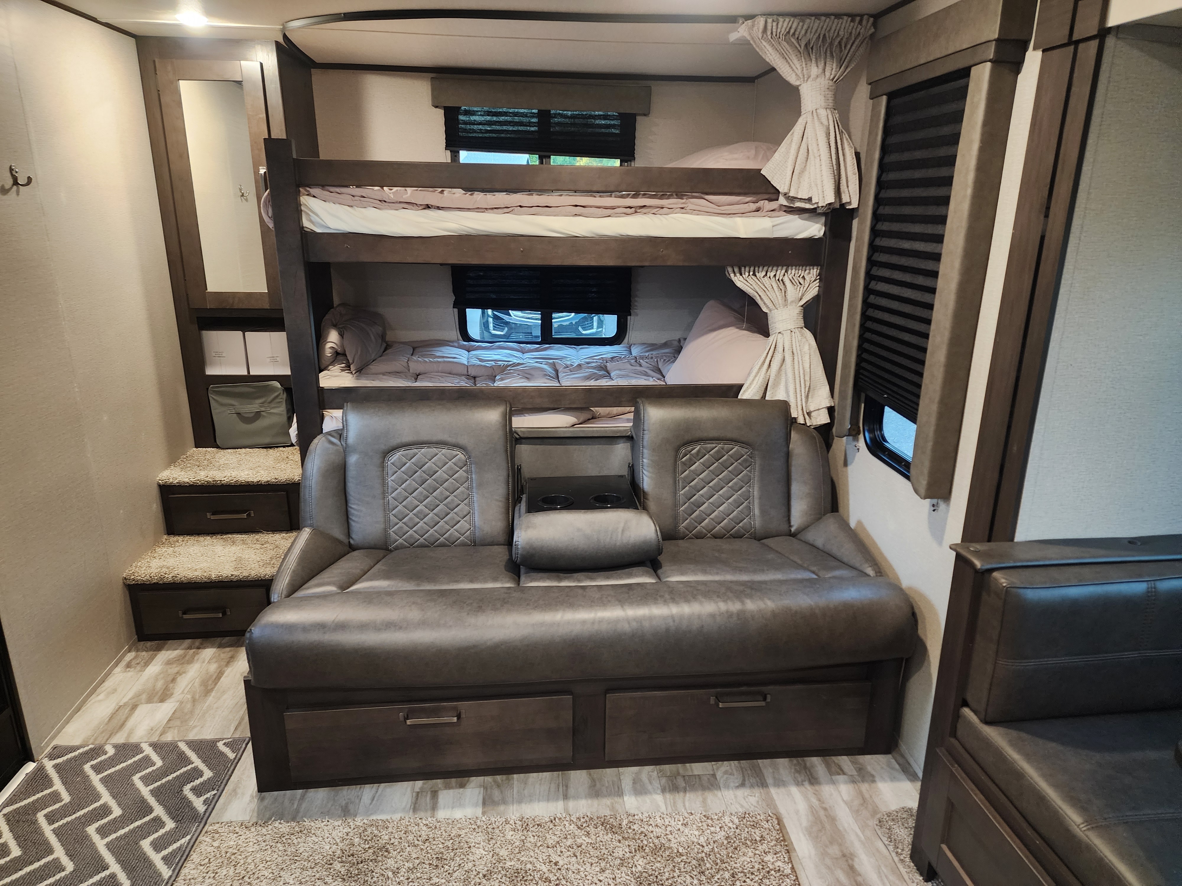 RV rental interior: comfortable bunk beds, grey sofa with cup holders, and steps with storage. Ideal for travel.. Grand Design Transcend Xplor 2022