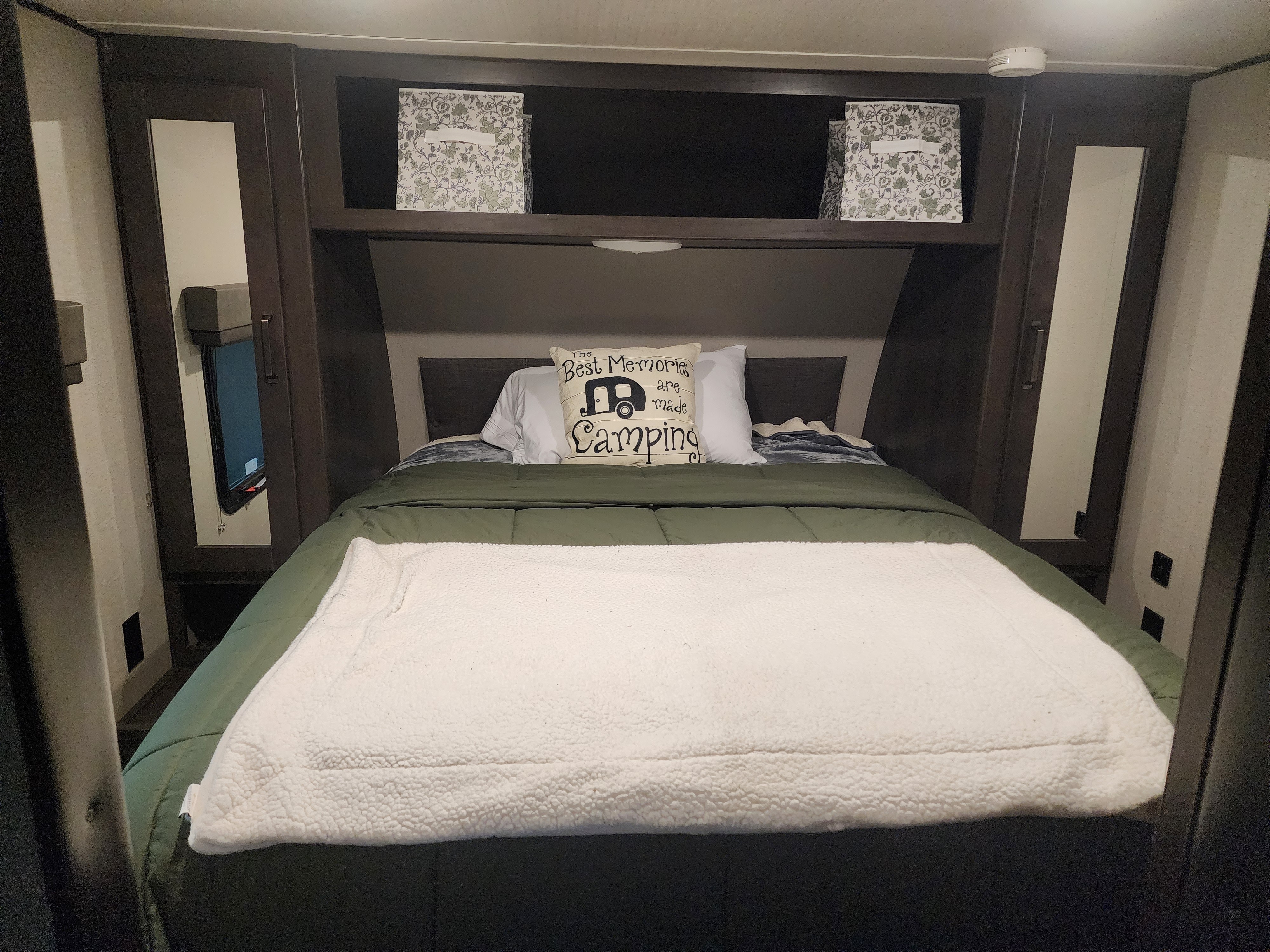 Cozy RV rental bedroom with a made bed, camping pillow, and overhead storage bins, ready for adventure.. Grand Design Transcend Xplor 2022