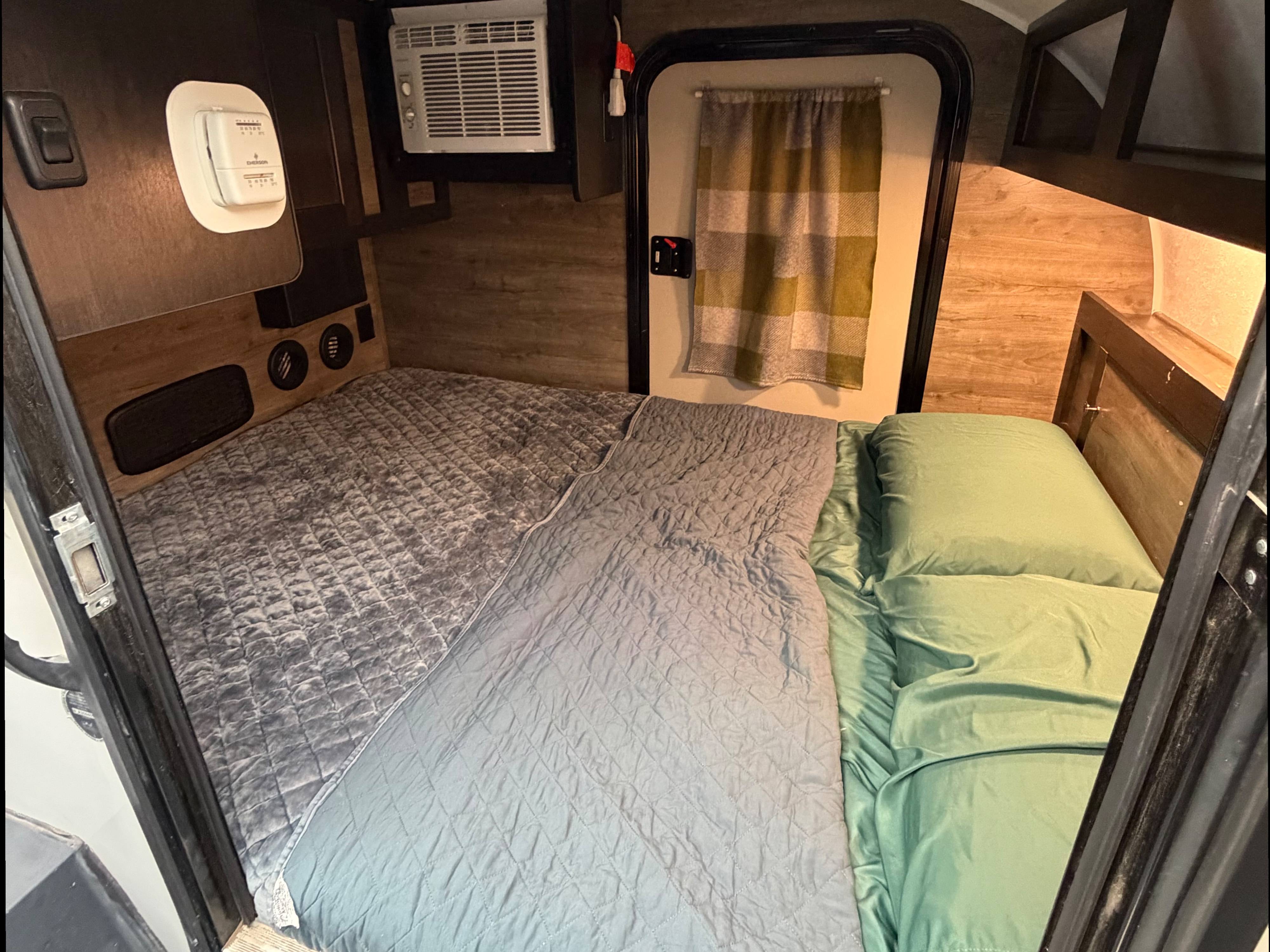 RV rental sleeping area: cozy bed, AC unit, thermostat, and plaid door curtain for comfort.. Braxton Creek Bushwhacker 2022