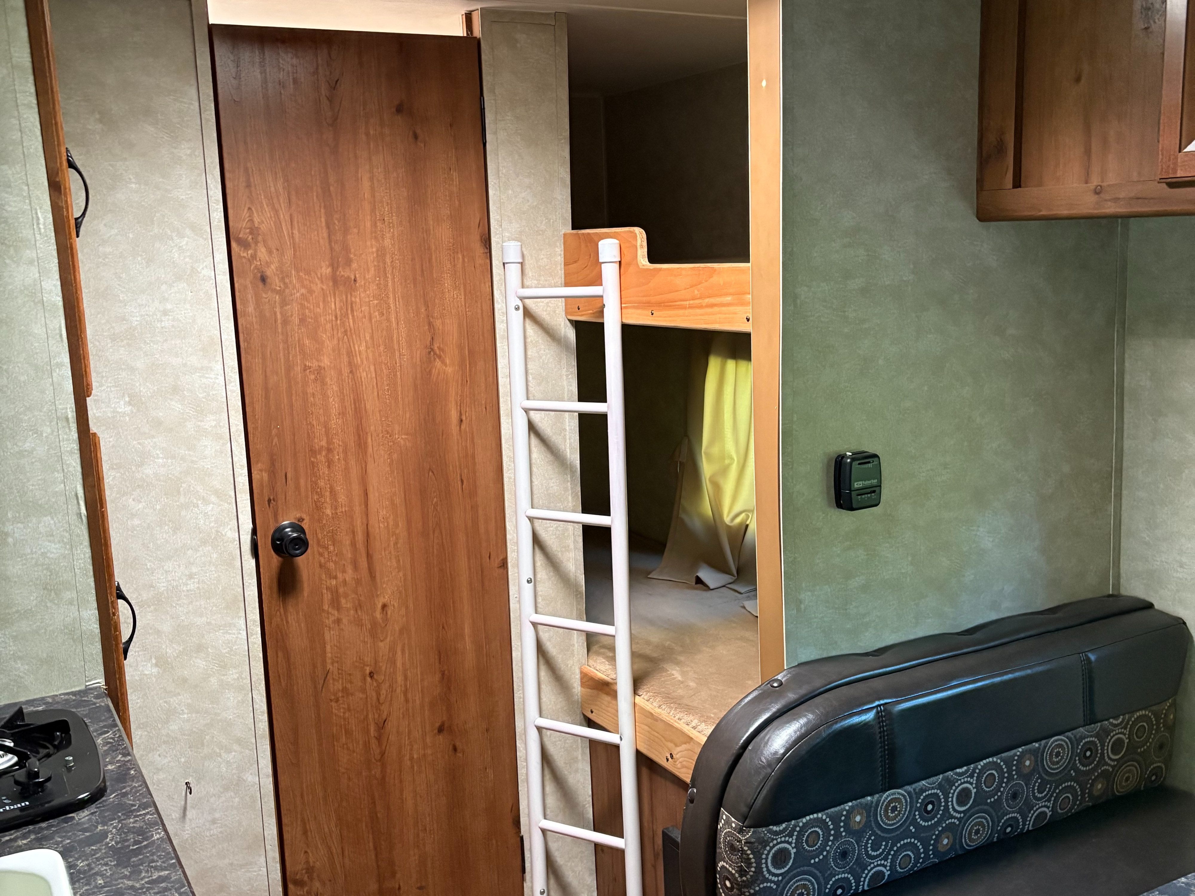 Interior of an **rv rental** showing bunk beds with a ladder, a wooden door, a compact kitchenette, and a patterned dinette seat.. Gulf Stream Ameri-Lite Super-Lite 2016