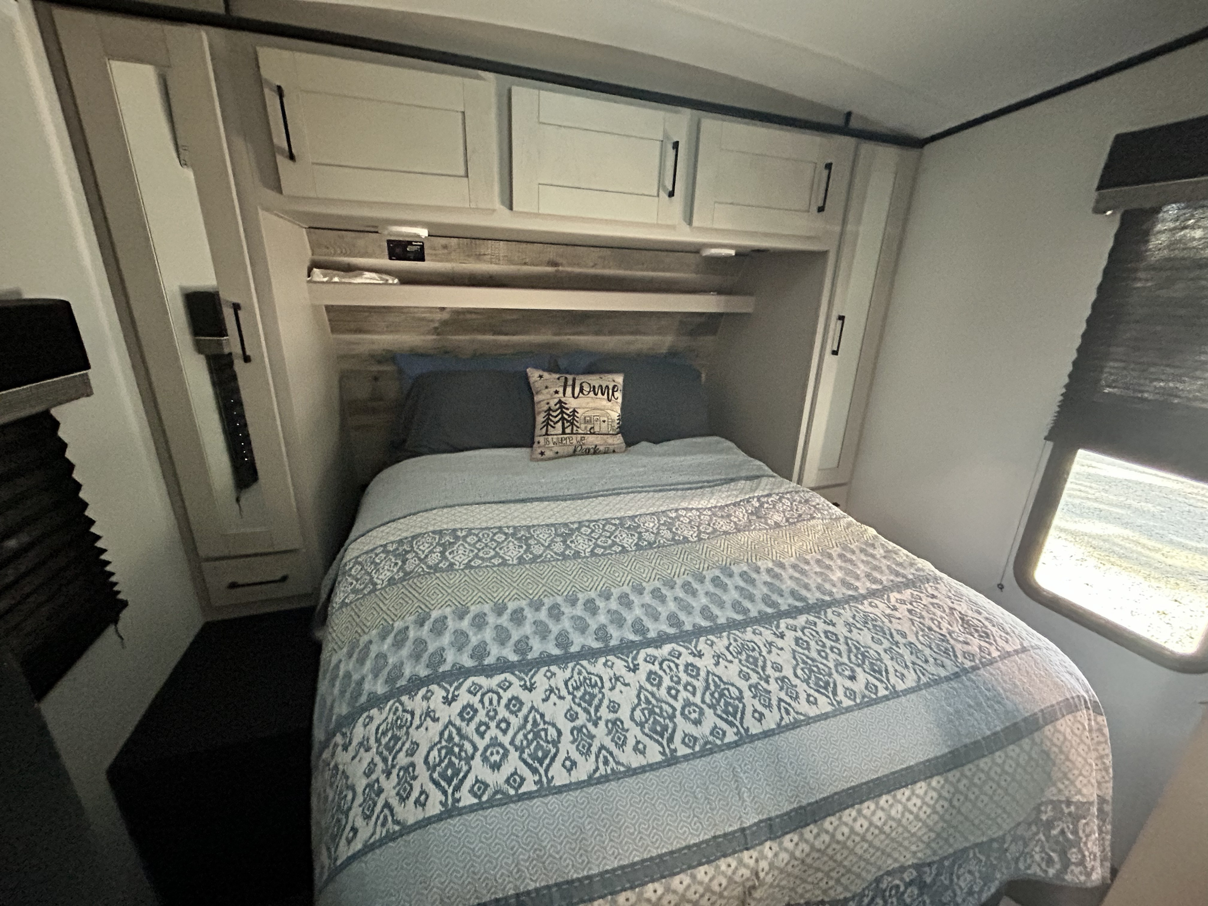 Cozy RV rental bedroom featuring a neatly made bed with patterned quilt, "Home" pillow, overhead storage, and window.. Heartland Torque 2021