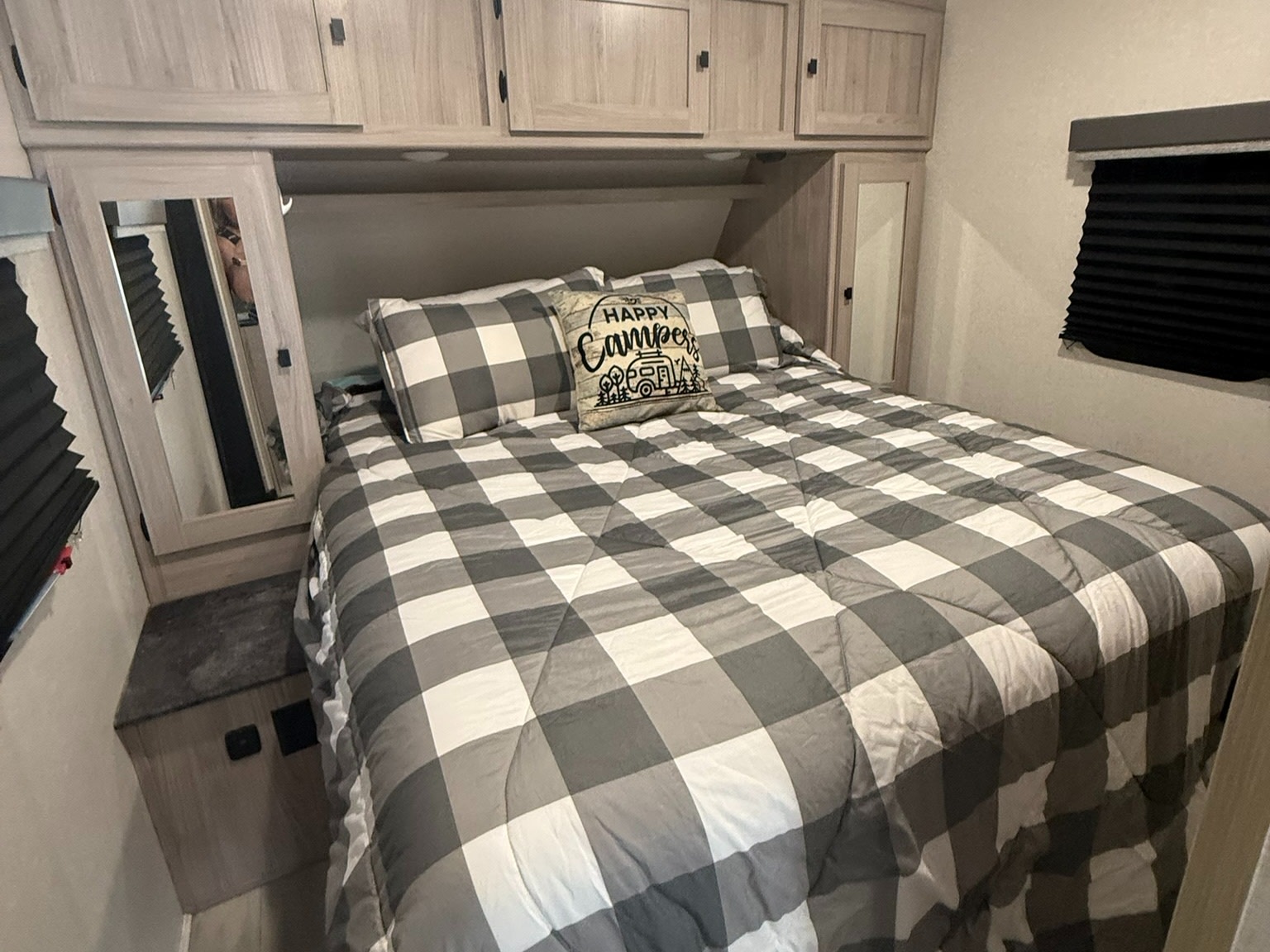 Inviting RV rental bedroom with checkered bedding, "Happy Camper" pillow, overhead cabinets, and a side mirror.. Coachmen Northern Spirit - 2557 RB 2023