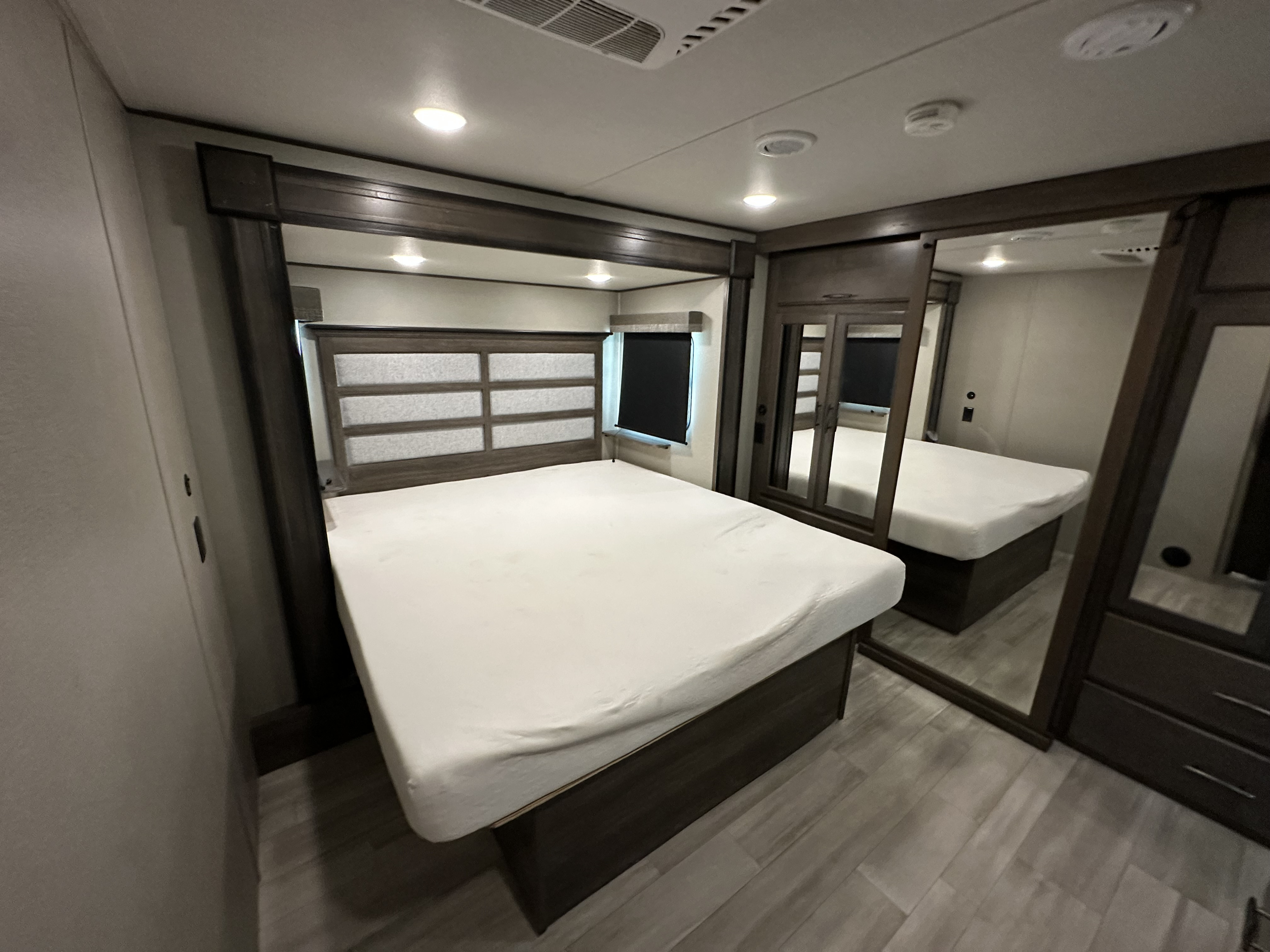 Inside a modern RV rental bedroom: large bed, stylish headboard, mirrored wardrobe, and window.. Grand Design Solitude 2023