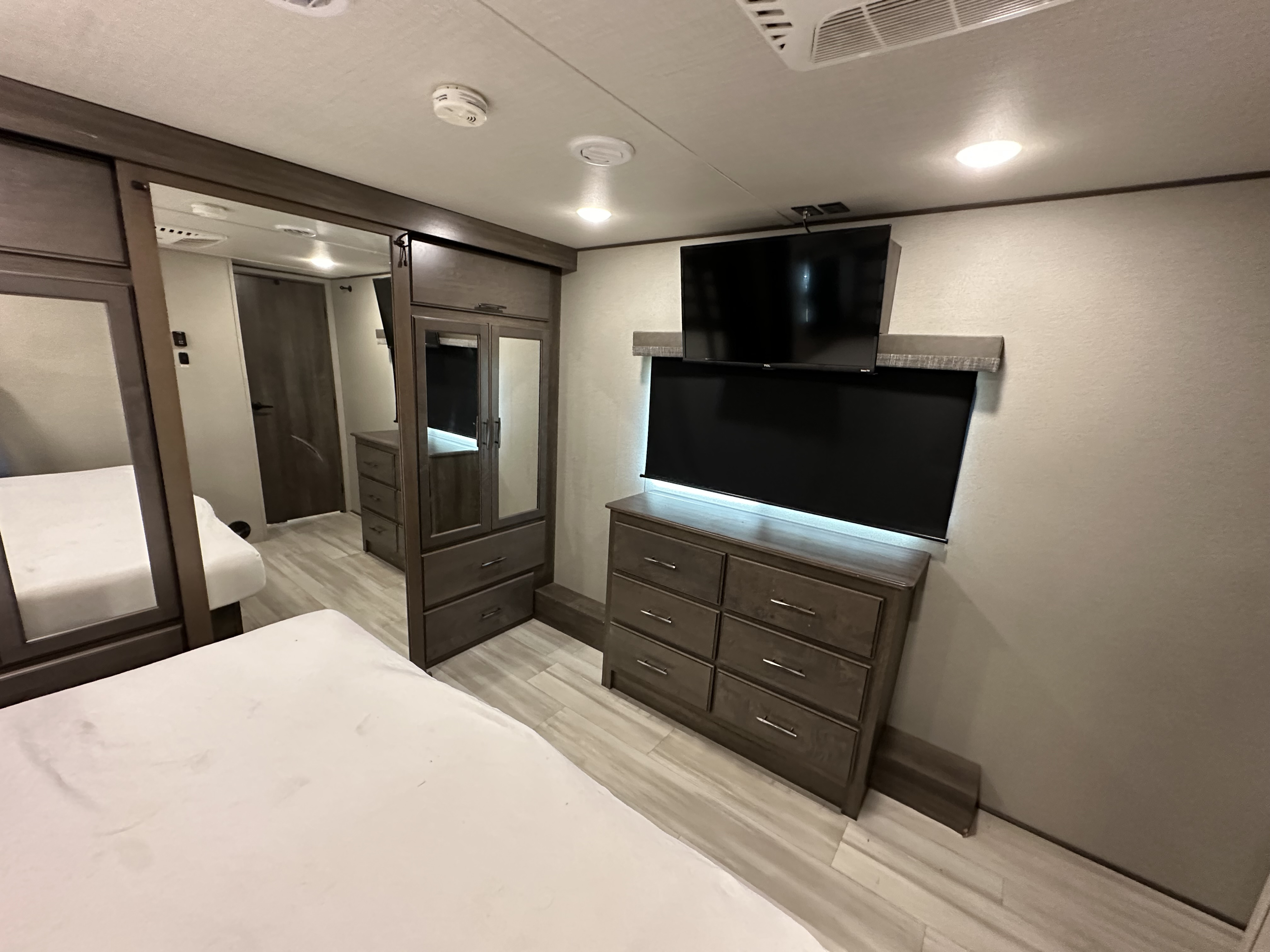 Modern RV rental bedroom showing a bed, dressers, TVs, and mirrored wardrobe, ideal for travel comfort.. Grand Design Solitude 2023