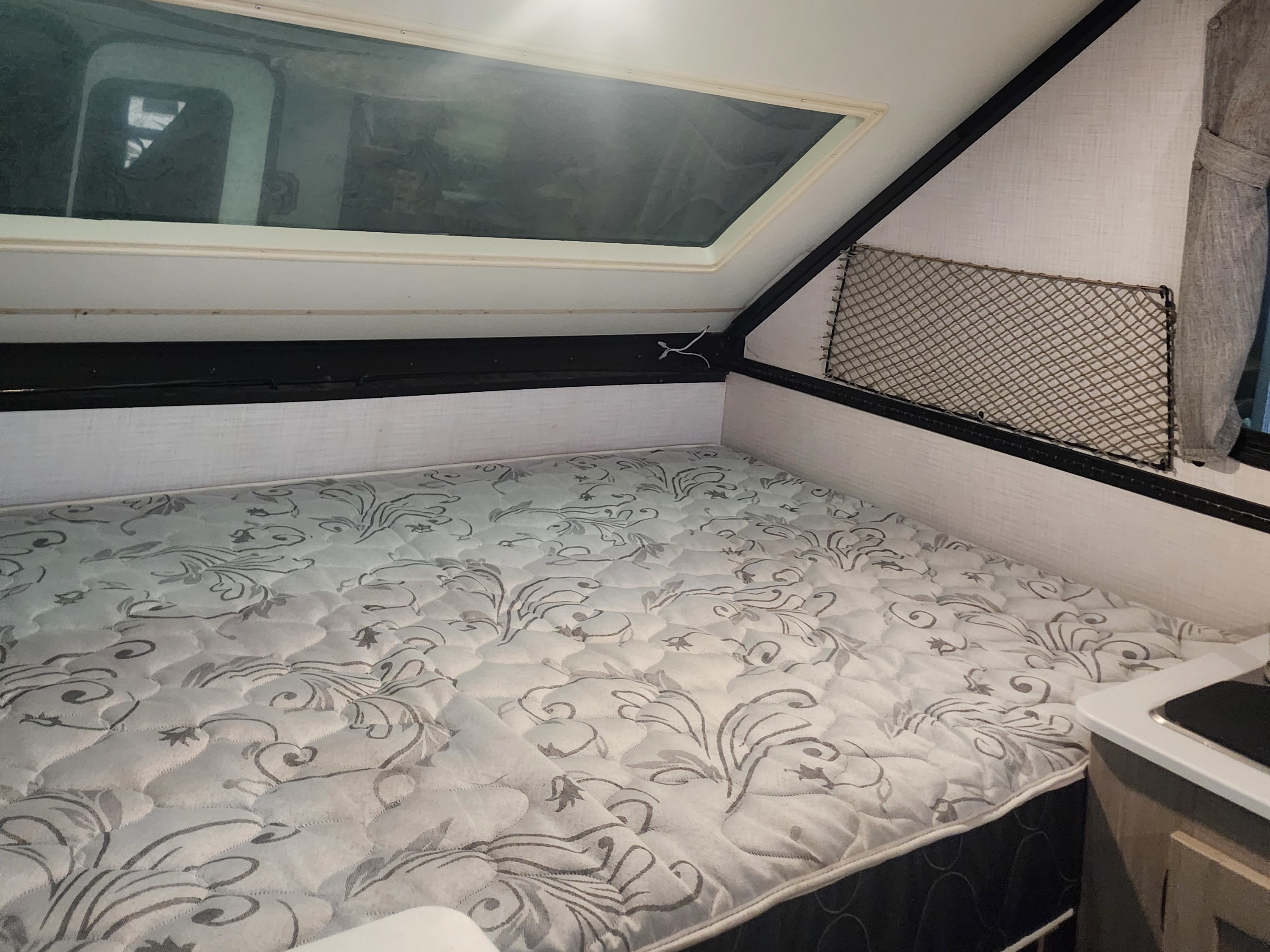 RV rental interior: A cozy sleeping area with a patterned mattress, overhead window/skylight, and storage net.. Forest River Rockwood ESP 2024