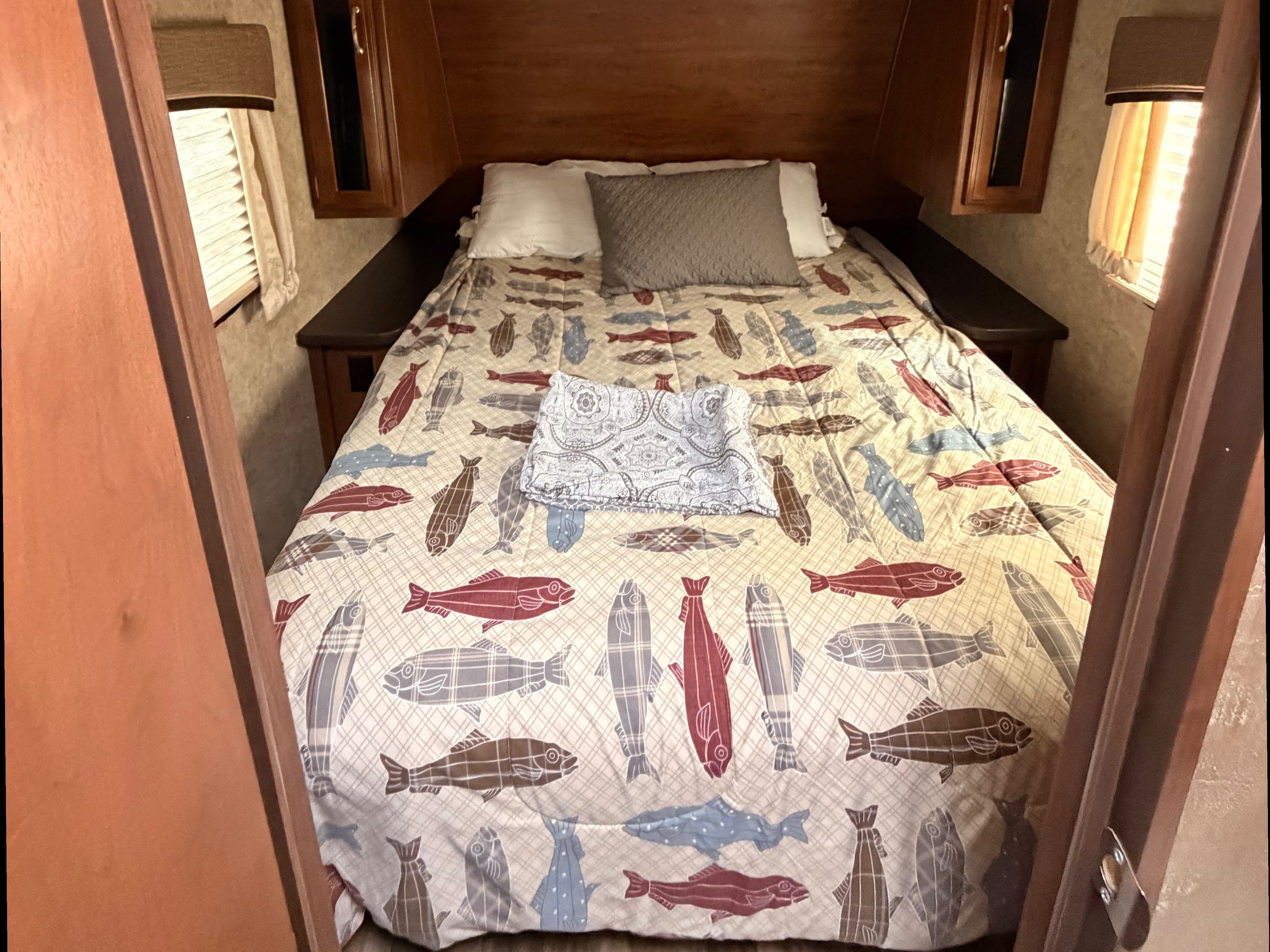 RV rental bedroom with a cozy bed, fish-patterned comforter, pillows, and wooden built-in storage.. Jayco Jay Feather 2017